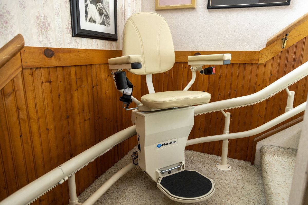 Stairlift chair on a carpeted stairway with wood-paneled walls and white handrails