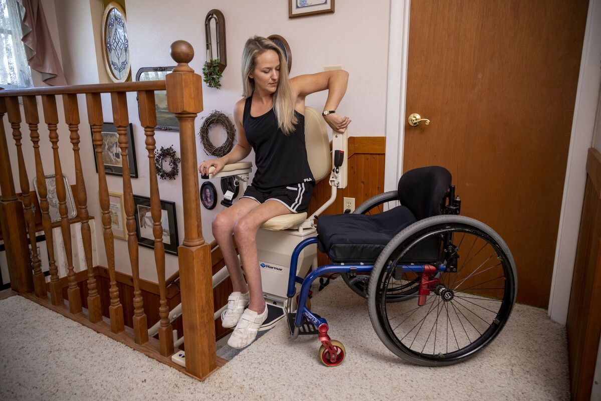 Woman sitting by a wheelchair on a staircase landing, looking at a smartphone.