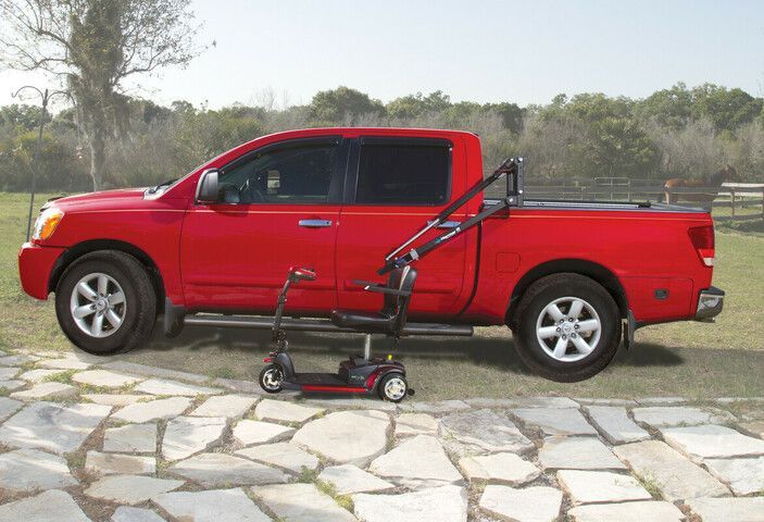 Red pickup truck with a golf push cart mounted in the bed, parked on a stone driveway.