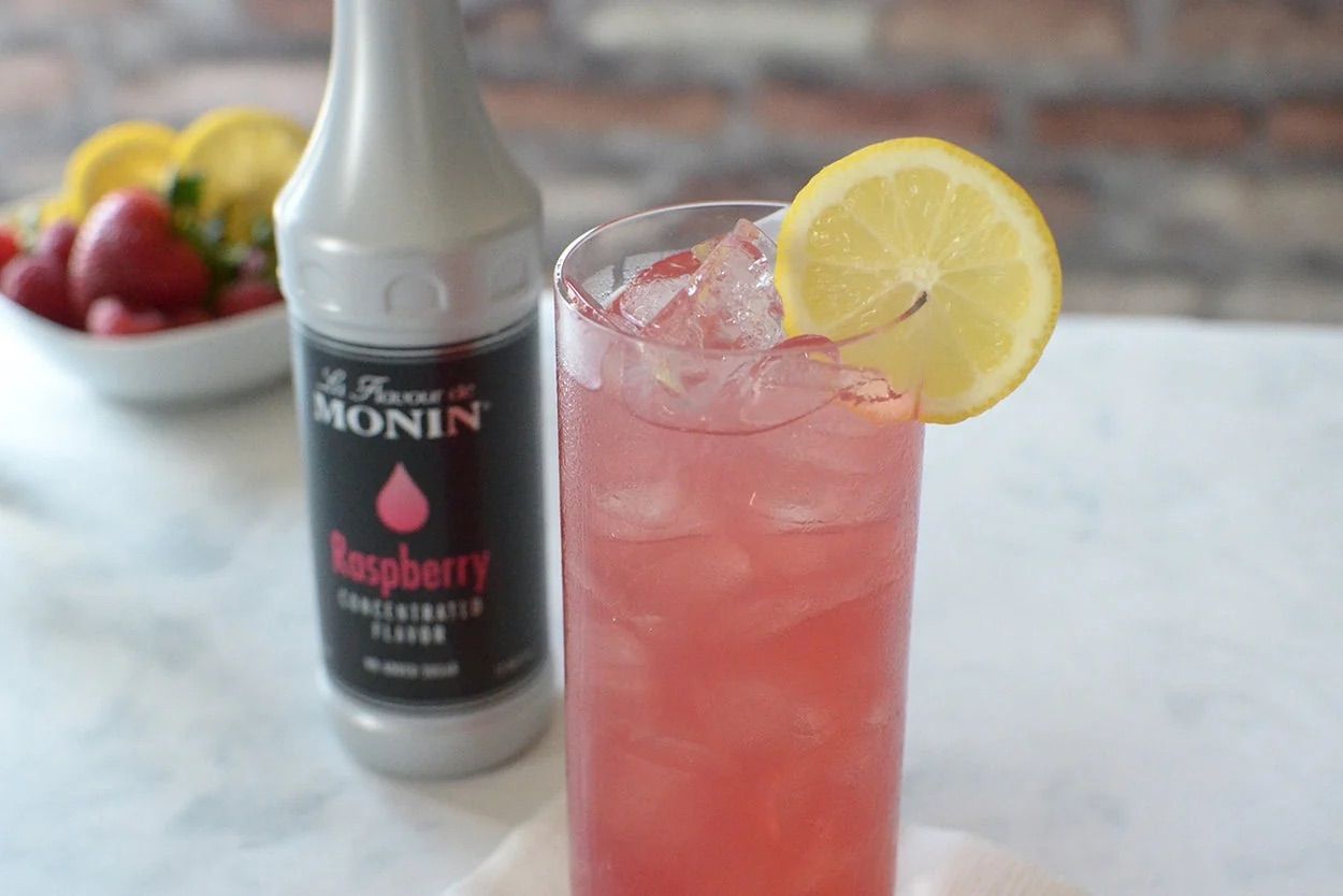 Bouteille de sirop de framboise Monin avec étiquette noire et touches de rose sur fond blanc