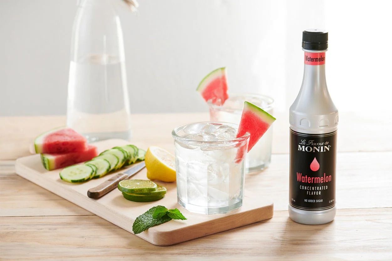 Bouteille de sirop aromatisé à la pastèque Monin avec bouchon noir et étiquette grise sur fond blanc