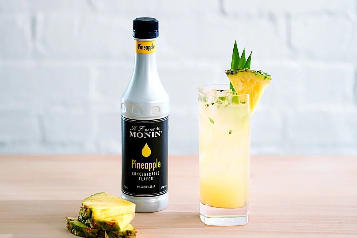 Bouteille de sirop d'ananas Monin avec étiquette noire et bouchon jaune sur fond blanc