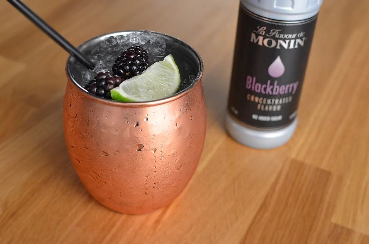 Bouteille de sirop de mûre Monin pour cocktail, avec étiquette noire et bouchon argenté sur fond blanc.