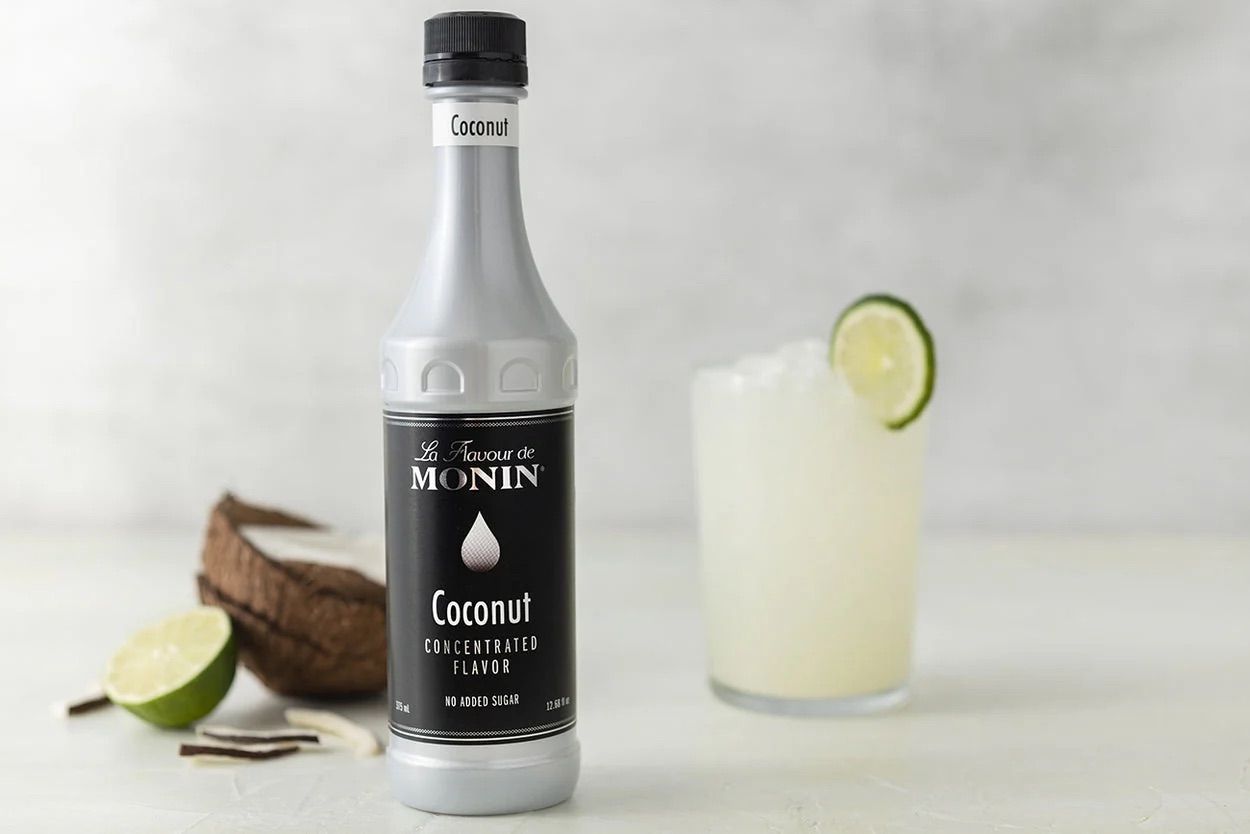 Bouteille de sirop de noix de coco Monin, en verre transparent avec étiquette et bouchon noirs sur fond blanc