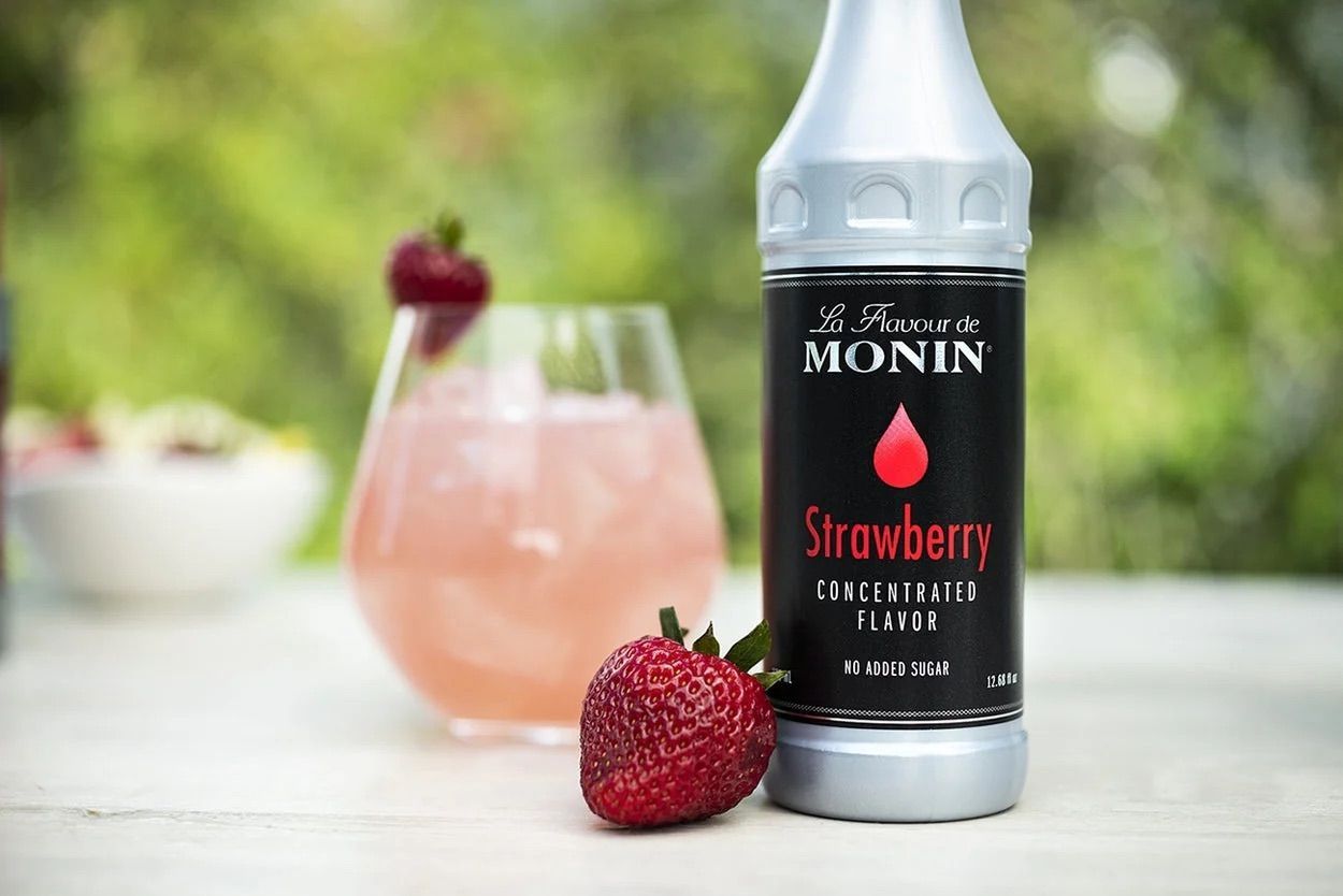 Bouteille de sirop de fraise Monin avec étiquette rouge et bouchon noir sur fond blanc