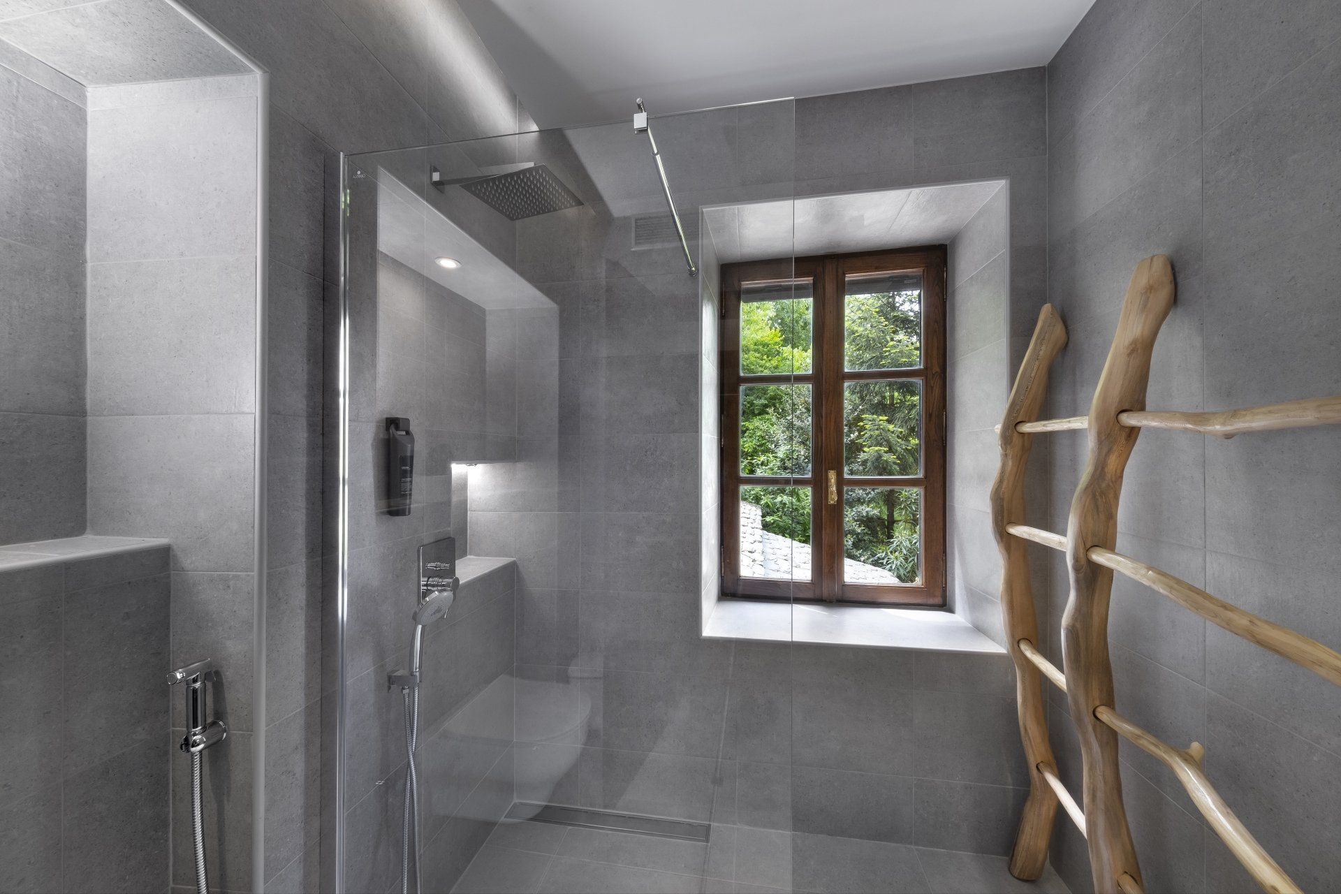Modern gray bathroom with shower, window, and wooden ladder-style towel rack.