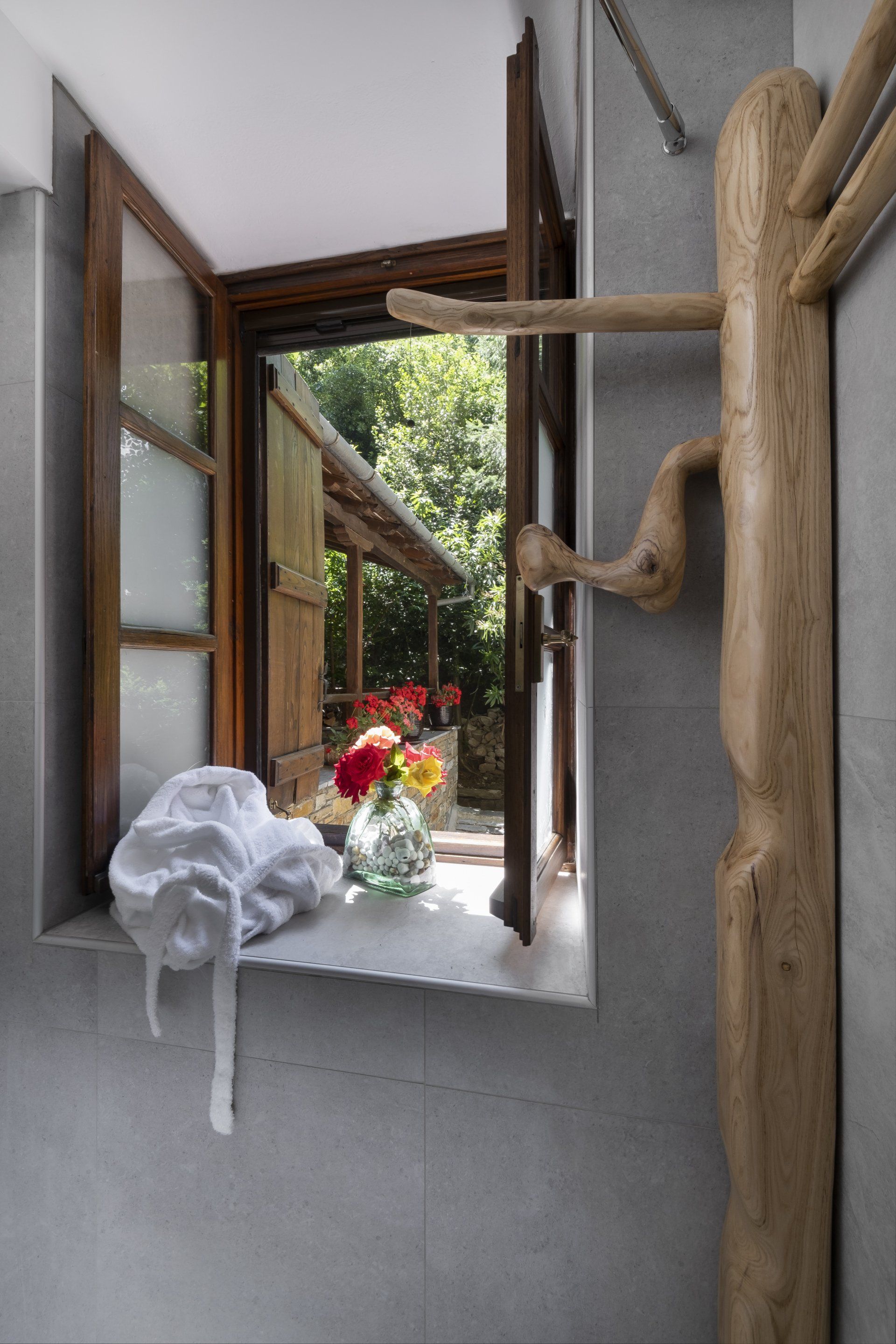 Window with a garden view, flowers in a vase, and a rustic wooden coat rack.