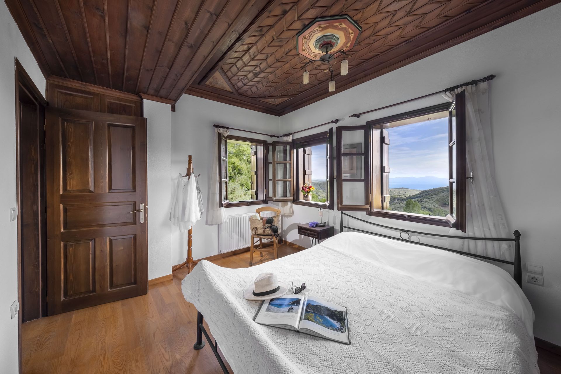 Bedroom with wooden ceiling, windows, and a bed with a hat and book.
