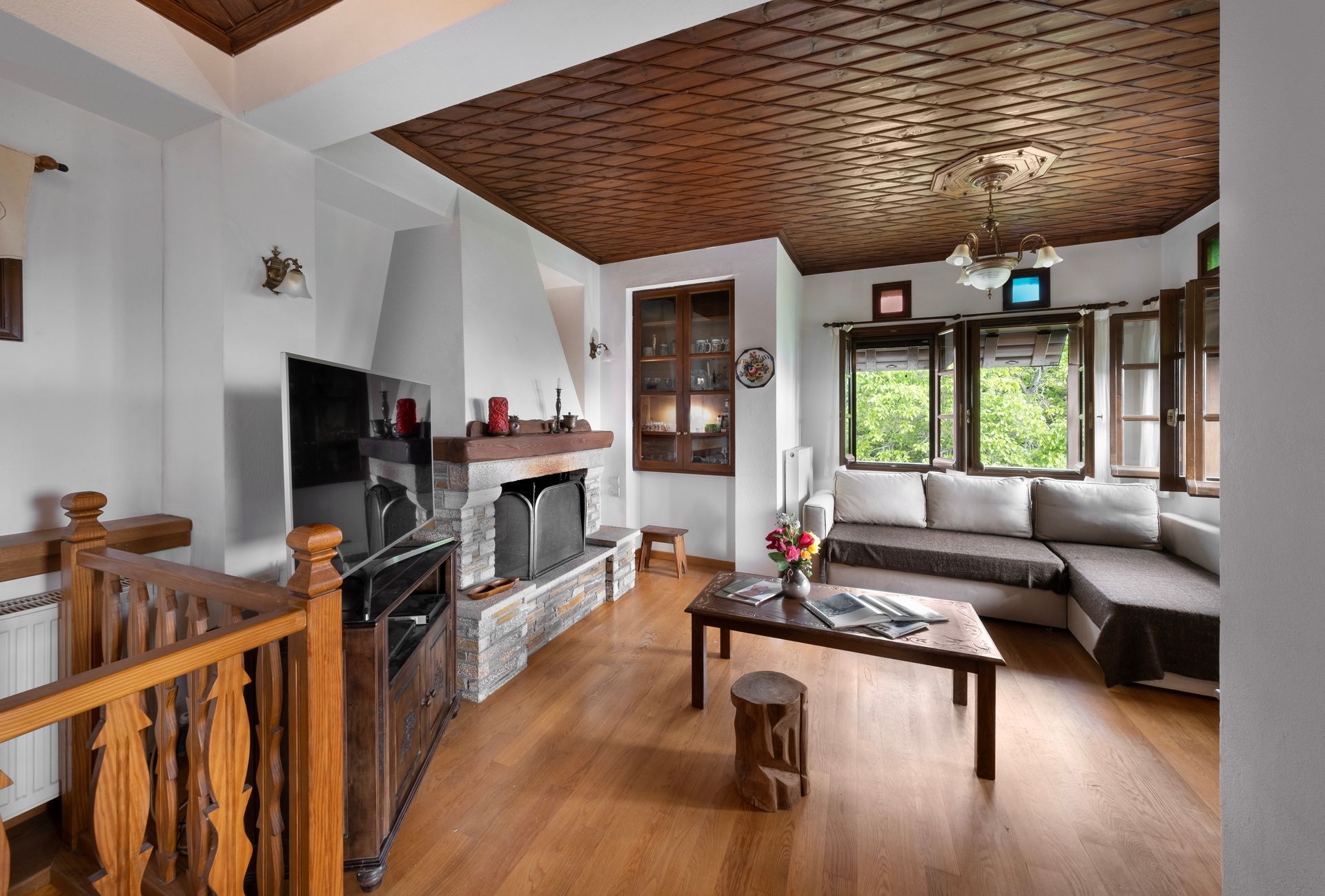 Cozy living room with fireplace, wooden ceiling, and sofa. Natural light streams from the windows.