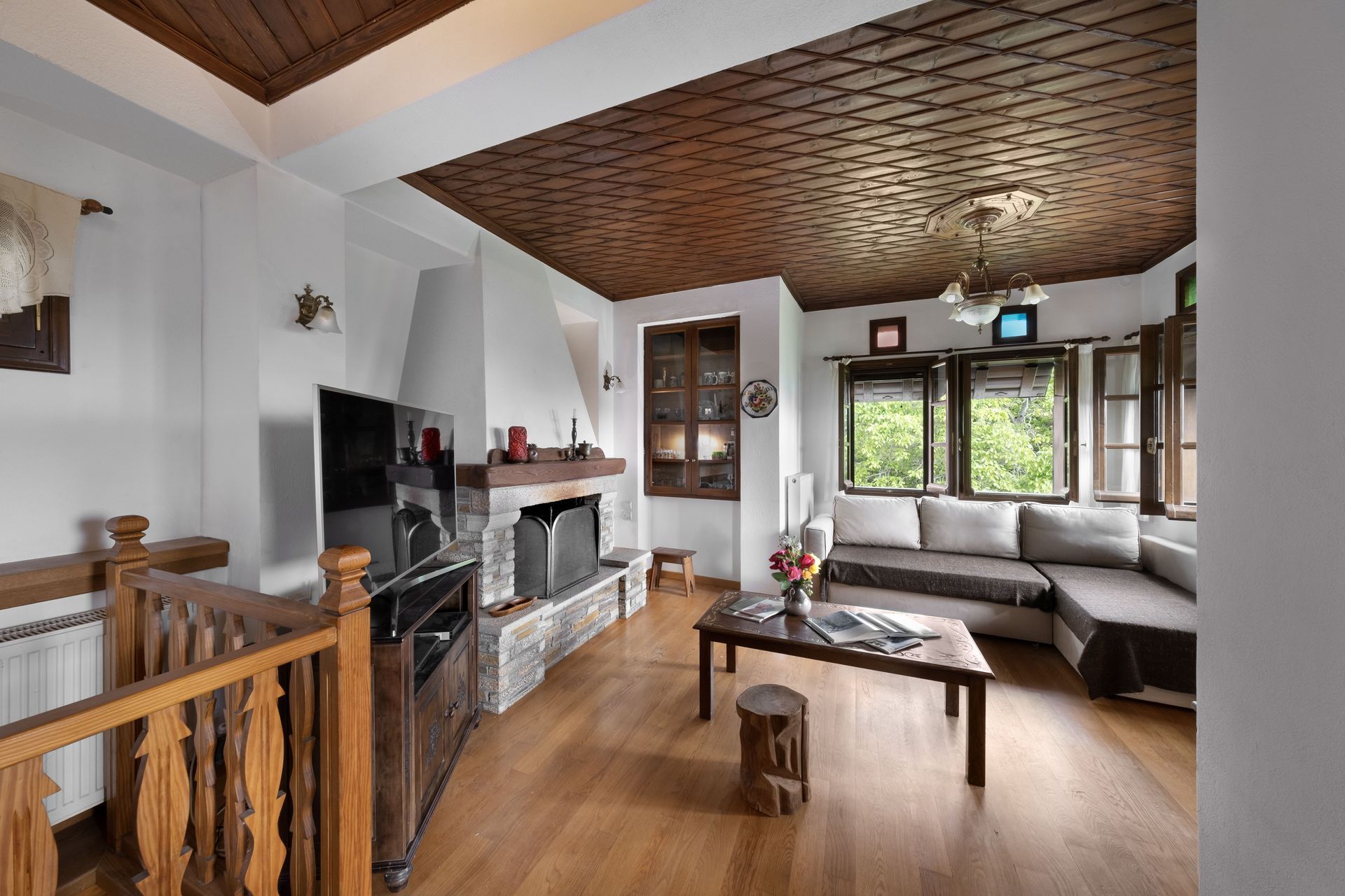 Living room with wooden ceiling, fireplace, sofa, and windows.