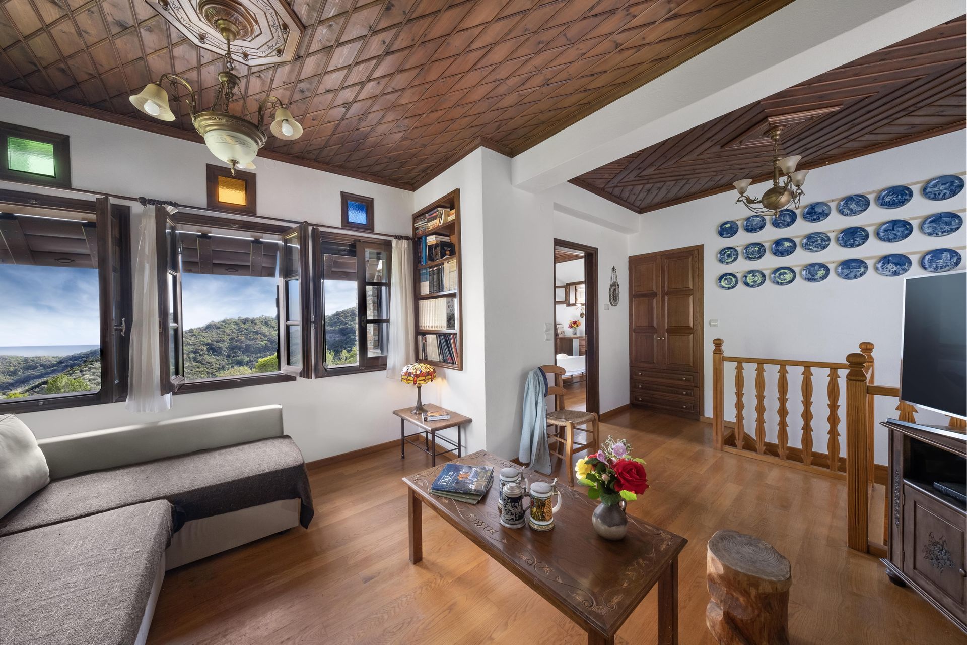 Living room with wooden floors, ceiling, and trim. Features a sofa, windows with a view, and decorative plates on the wall.