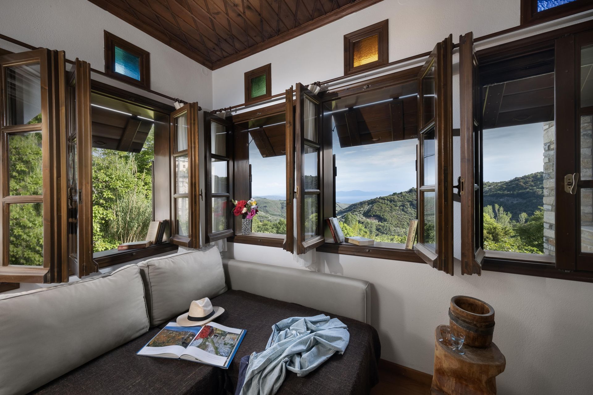 Cozy indoor seating area with open windows overlooking a lush, green landscape and distant body of water.
