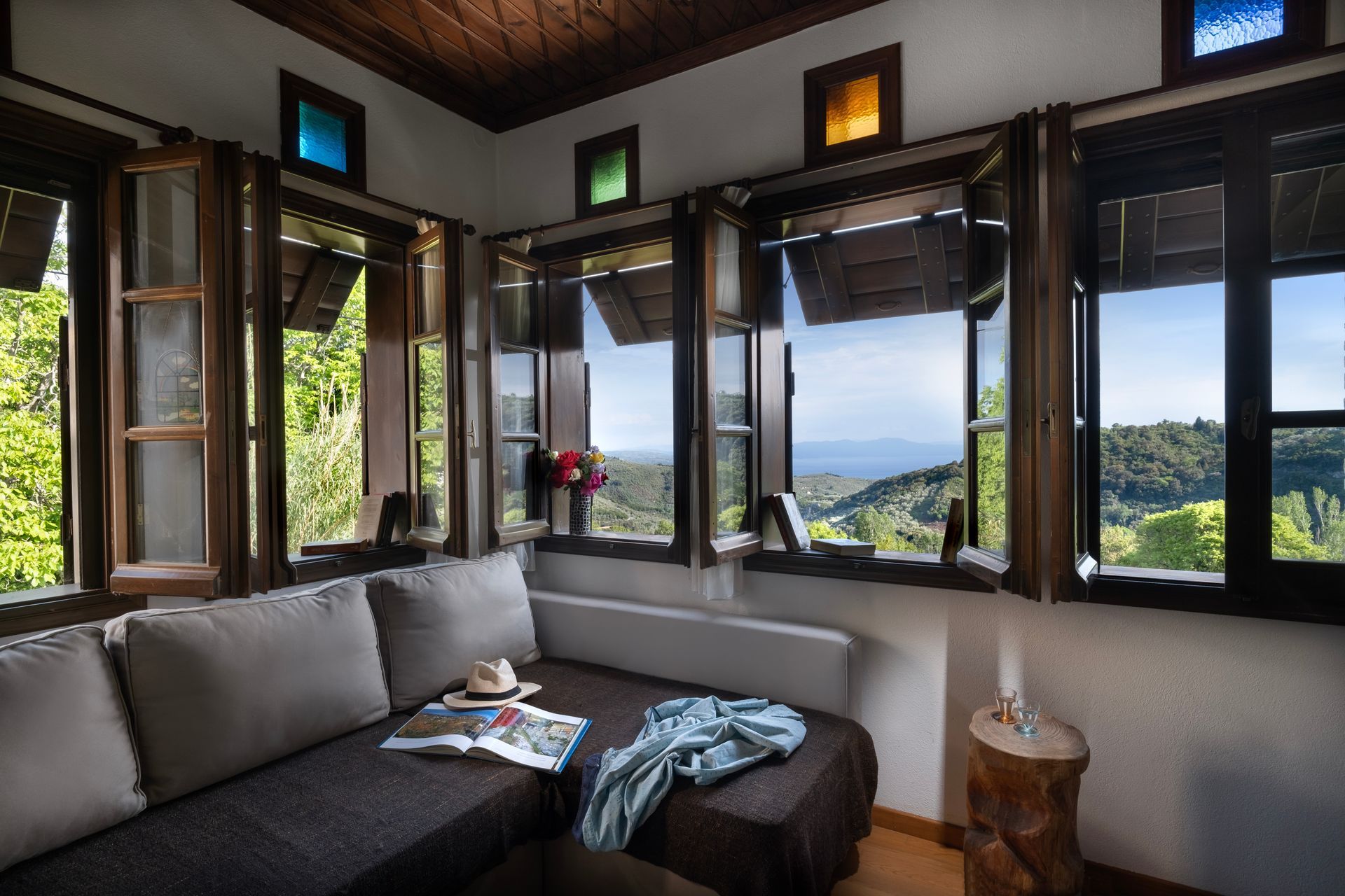 Cozy room with a couch and windows overlooking a scenic mountain view. Brown wooden trim. Sunlight.