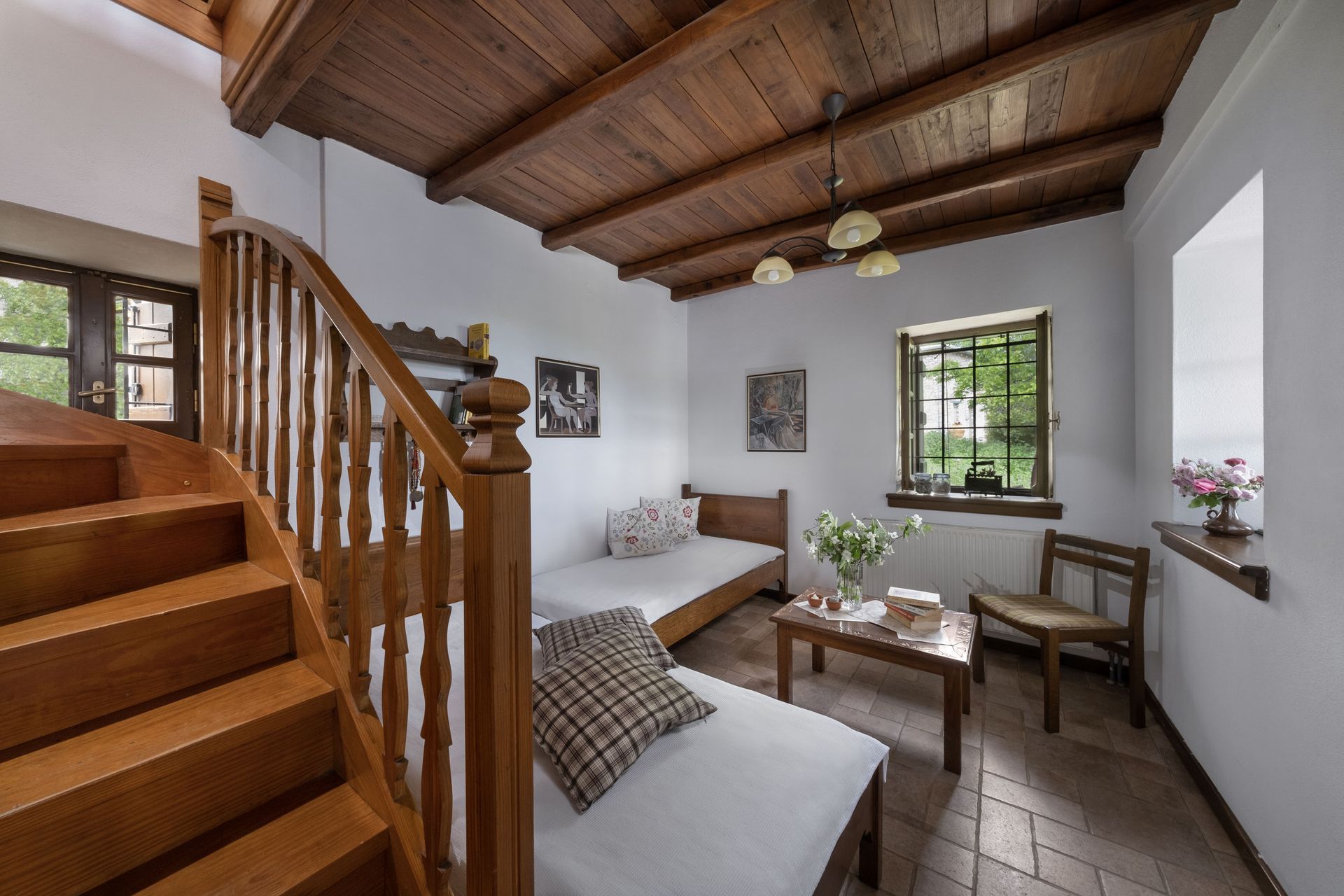 Wooden staircase leads up to a bright room with two beds, small table, and a window.