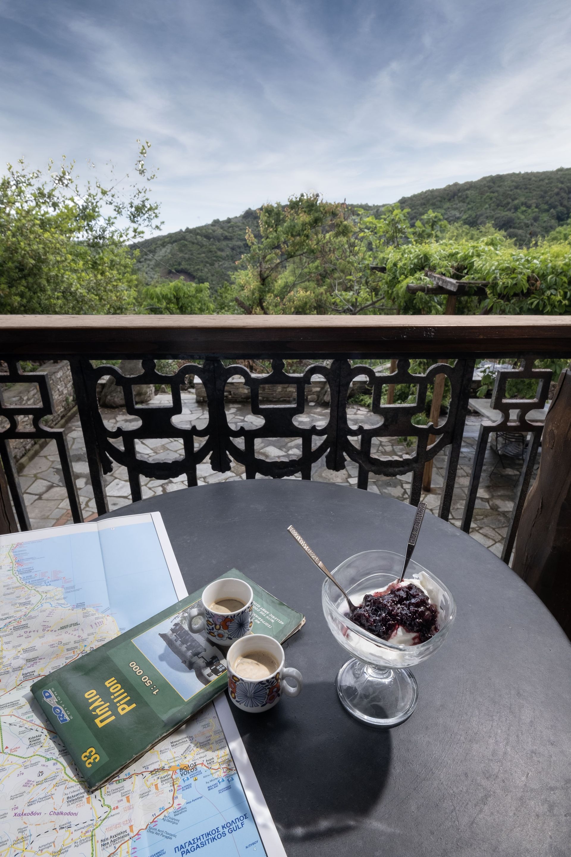 Table set for one with dessert, coffee, map, overlooking a green landscape and blue sky.