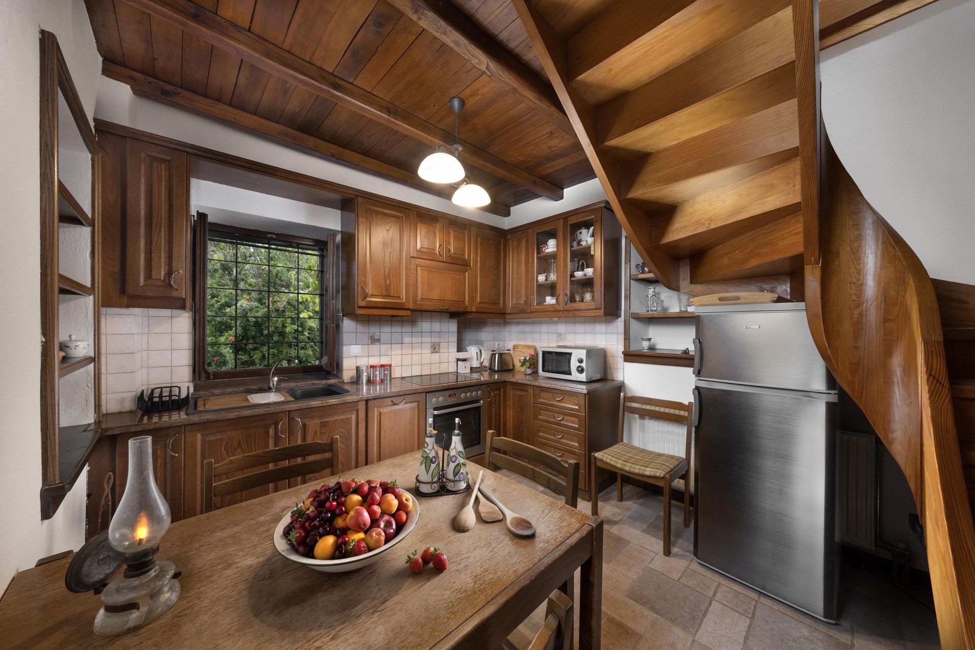 Wooden kitchen with a spiral staircase, cabinets, and a table with fruit.