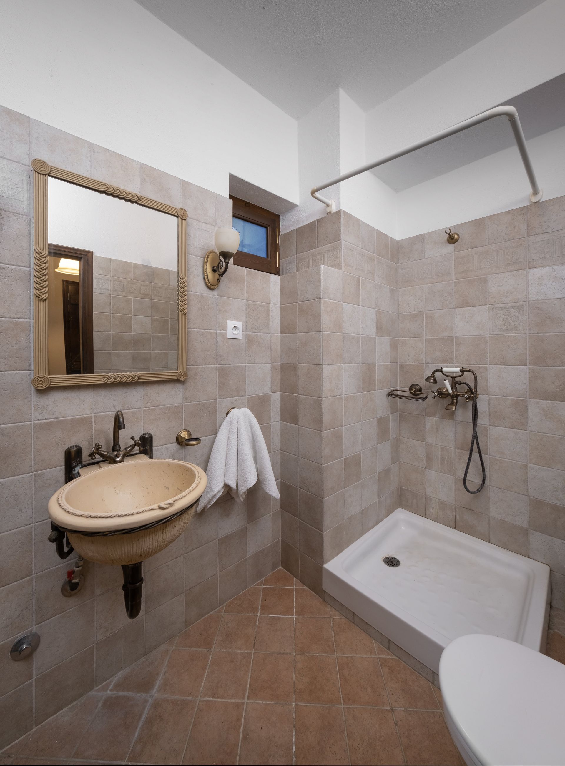 Bathroom with beige tile walls and floor, shower, sink with ornate mirror, and toilet.