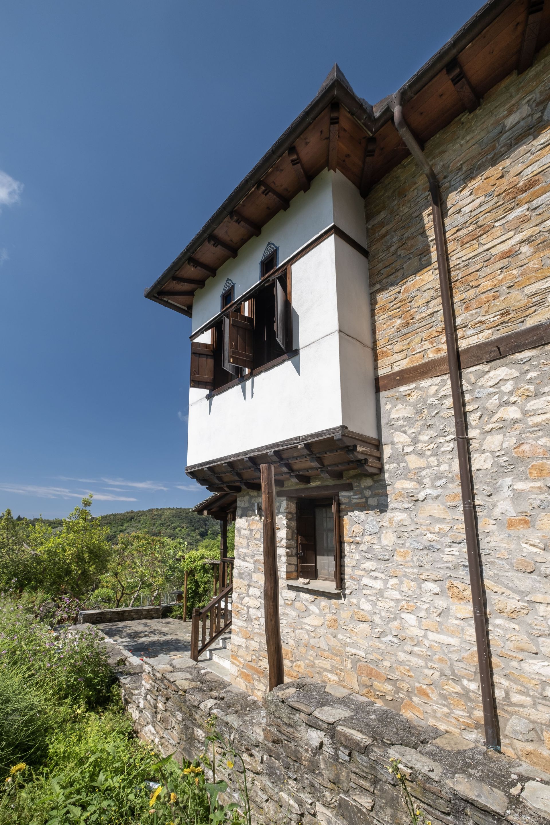 Stone and white building with a wooden balcony, set against a blue sky and greenery.