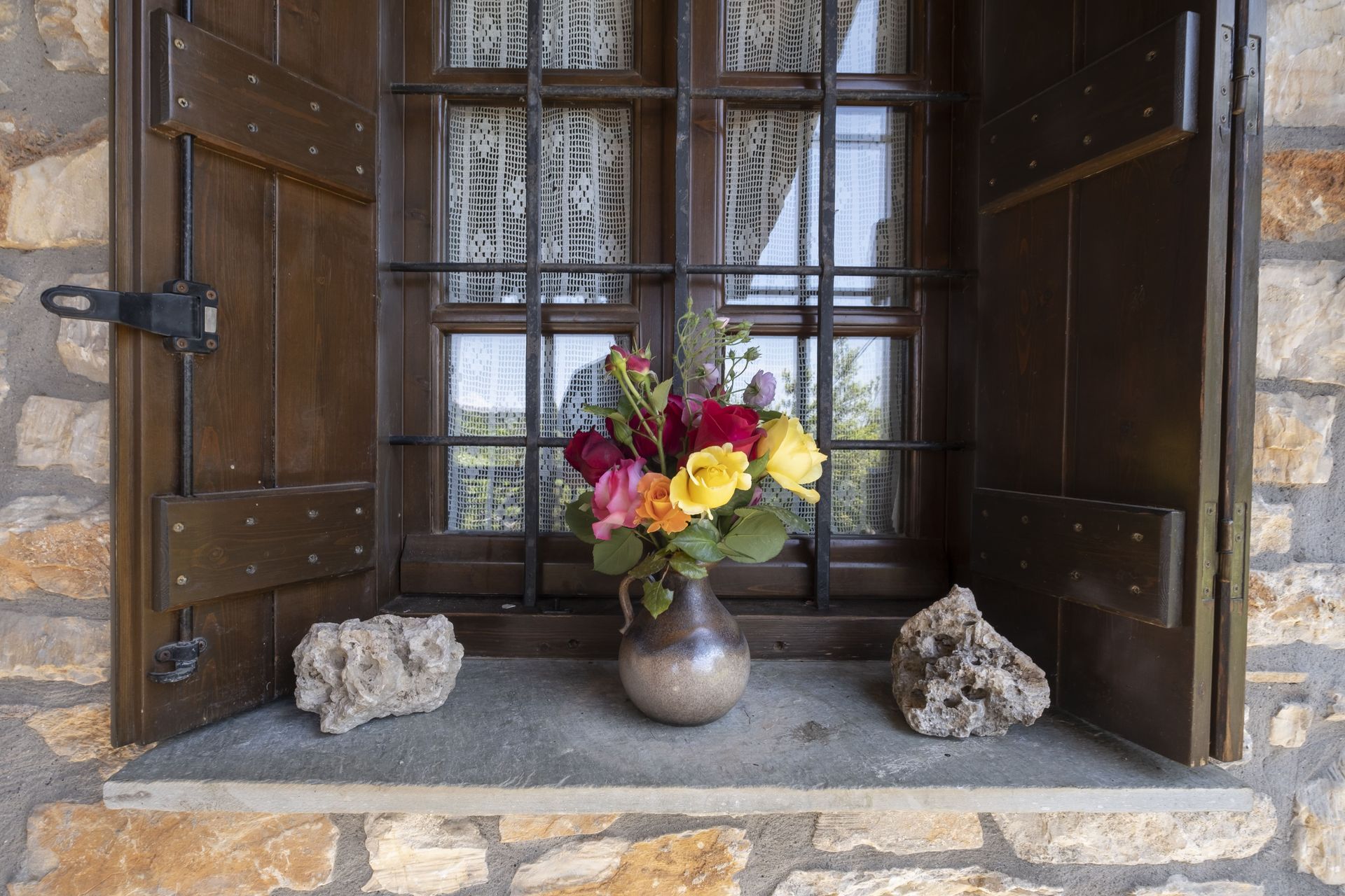 Flowers in vase on windowsill with stone accents, window with shutters and security bars.