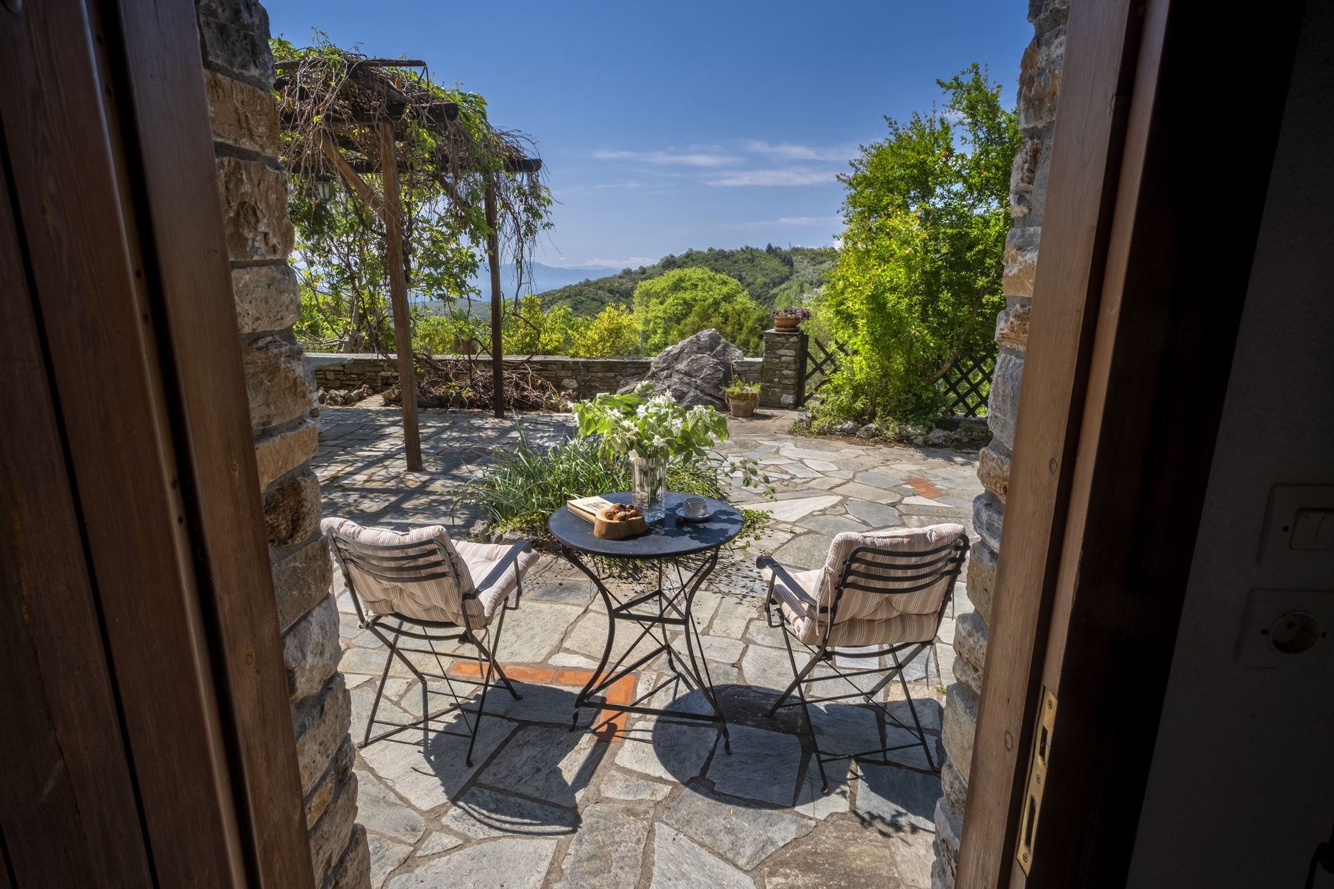 Stone patio with two chairs, small table, and scenic view seen through a doorway.