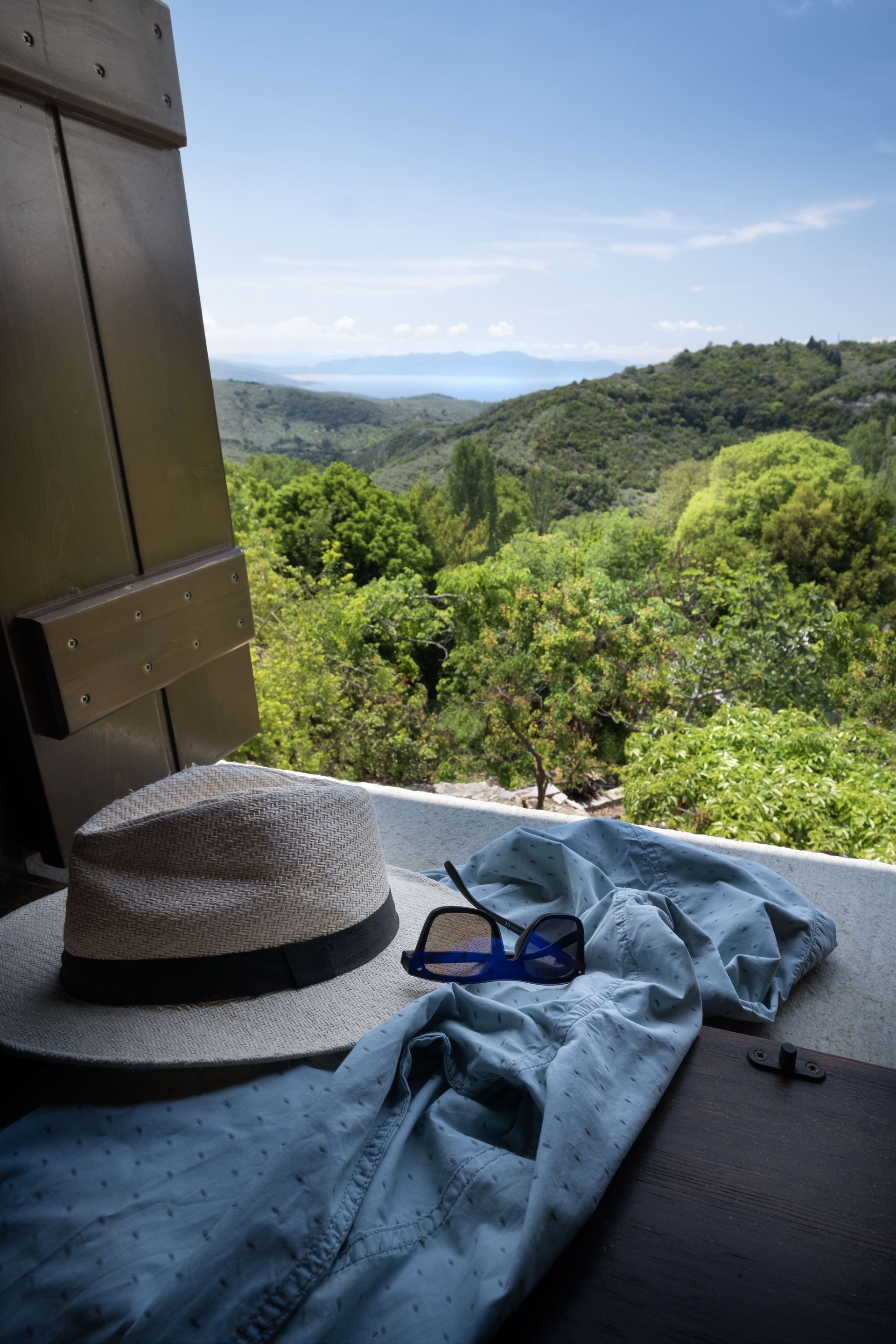 Hat, sunglasses, and shirt on a ledge, overlooking a green valley and blue sky.