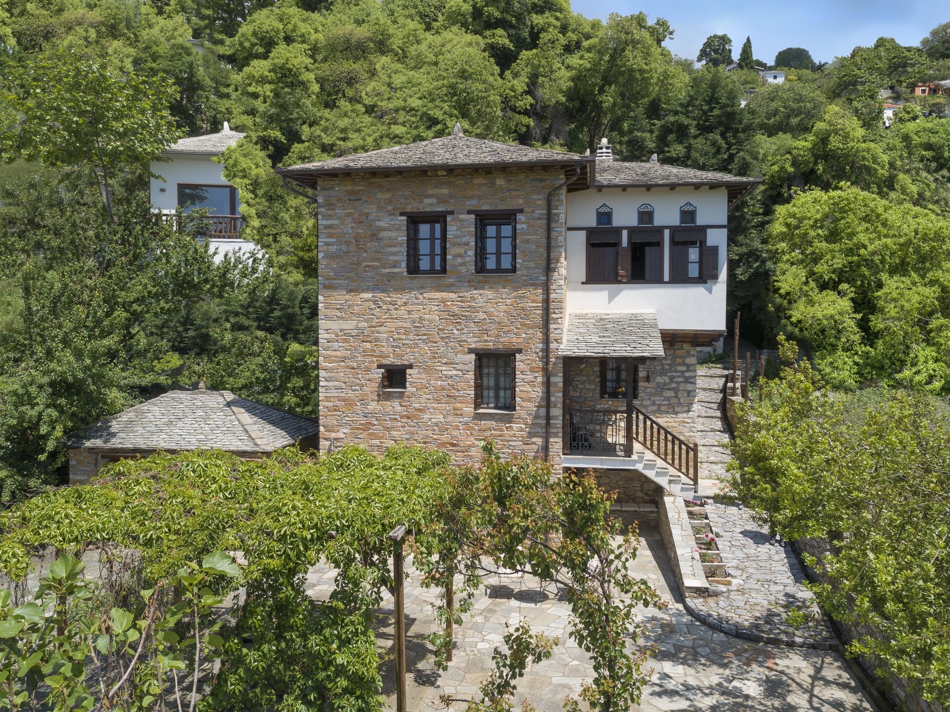 Stone and whitewashed two-story house with a slate roof in a lush green hillside setting.
