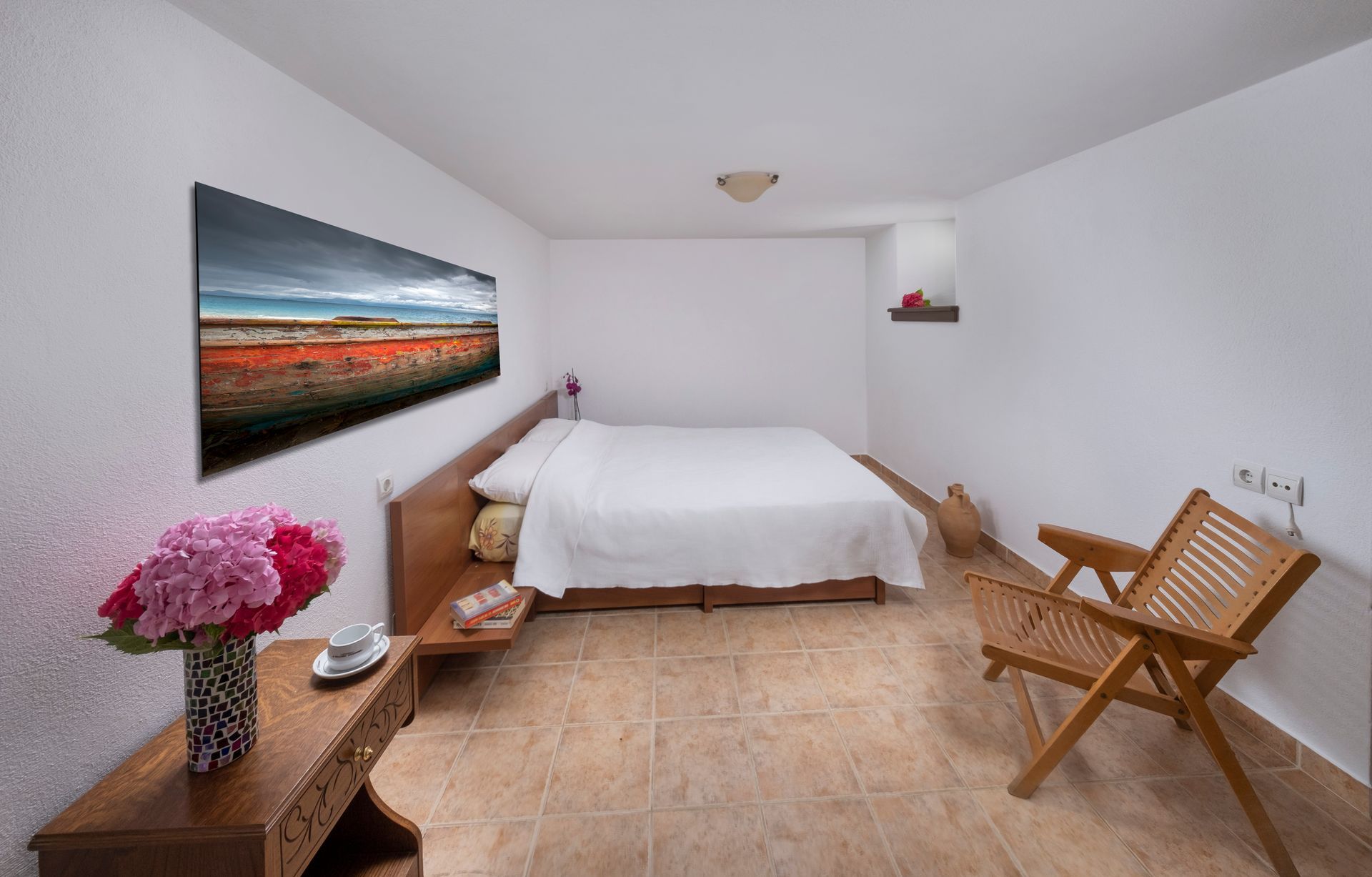 Bedroom with bed, painting, wooden furniture, and flowers.
