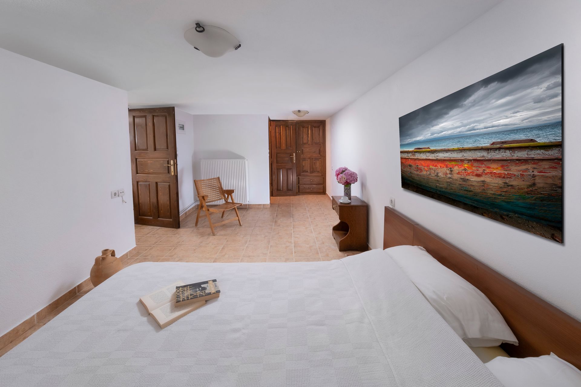Bedroom with a large bed, landscape artwork, wooden doors, and chair.