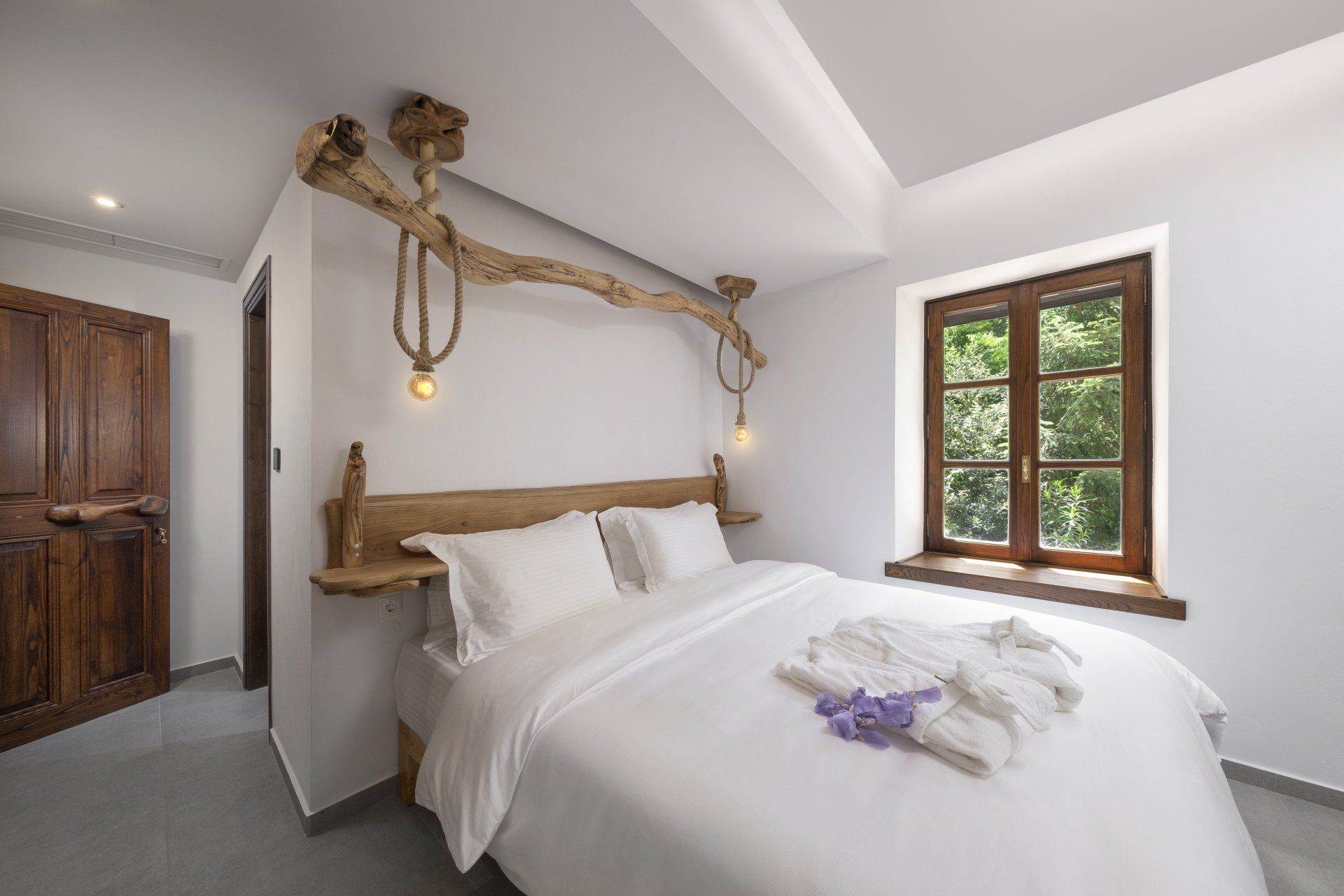 Bedroom with a bed, wooden headboard and accent lighting, and a window with a view of greenery.