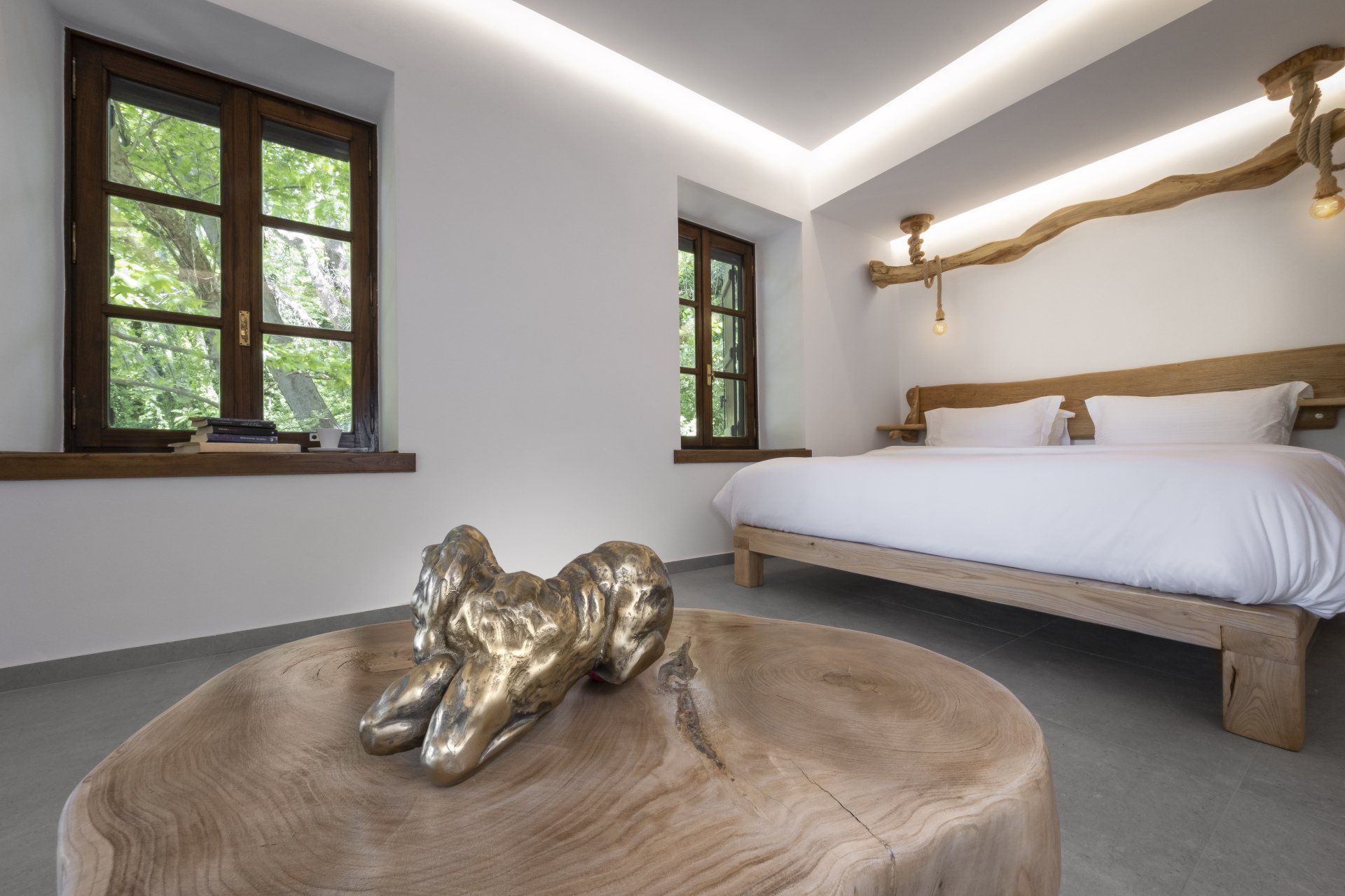 Bedroom with a wooden bed, coffee table with a sculpture, and two windows.