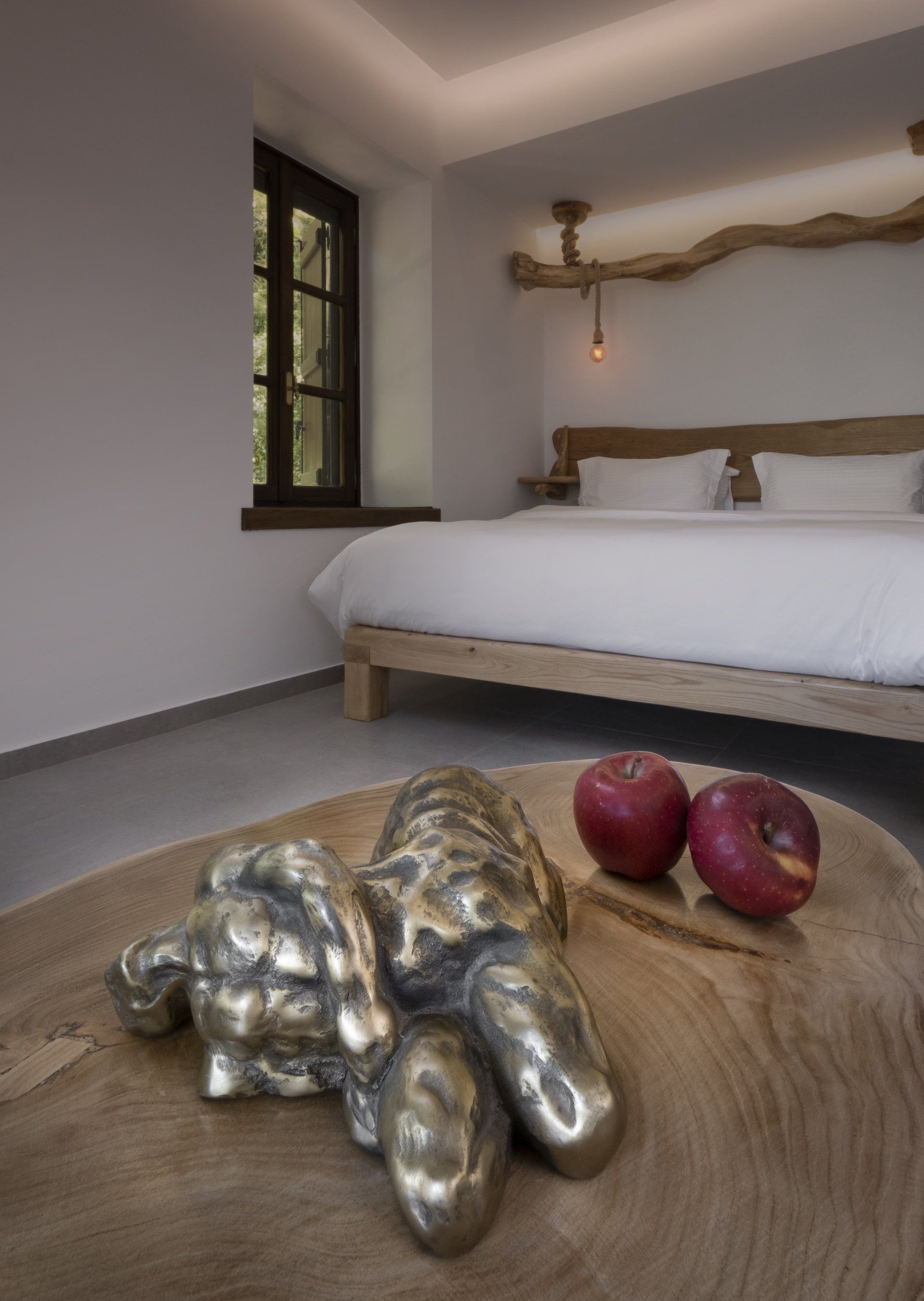 Bedroom interior with a wooden bed, sculpture on a wood table, and two red apples.