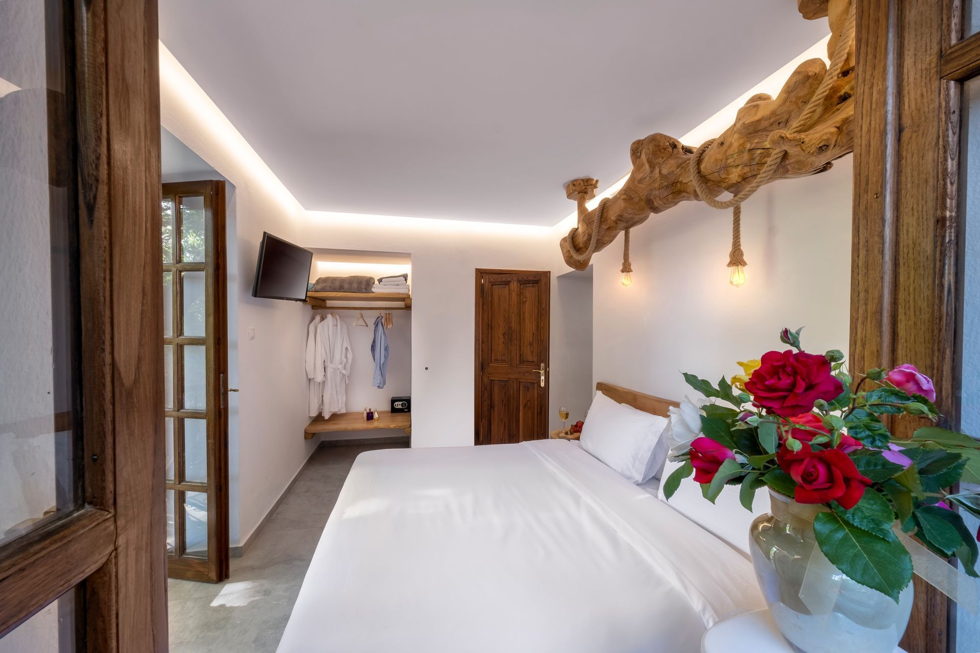 Bedroom with a double bed, open door, and a wooden beam above. A vase of roses is in the foreground.