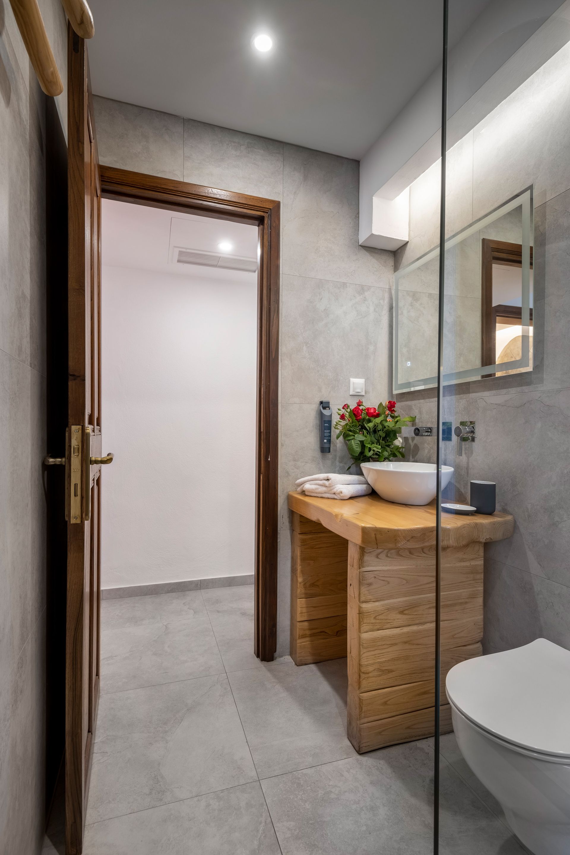 Bathroom with wooden vanity, white sink, toilet, and open door to a hallway with gray walls.