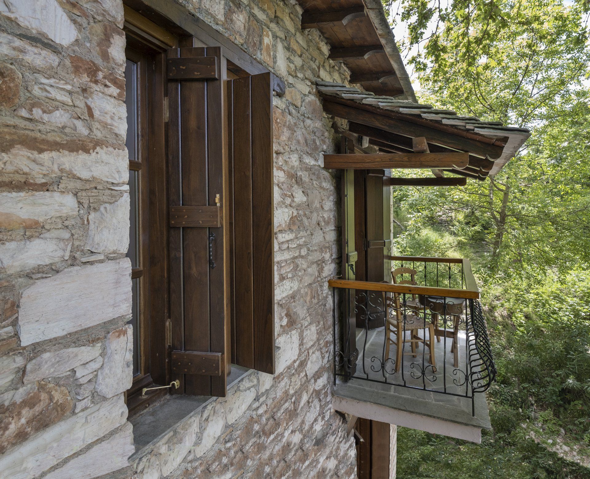 Stone building exterior with wooden shutters and balcony overlooking trees.