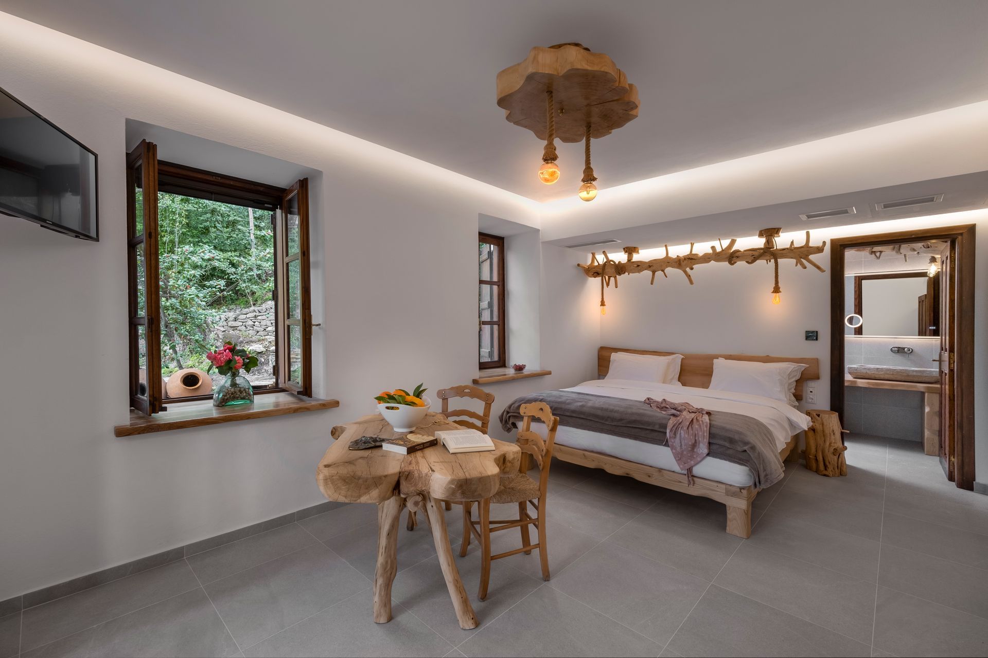 Bedroom with wooden furniture, bed, table, and tree-branch lighting. Bright, white walls with a window.
