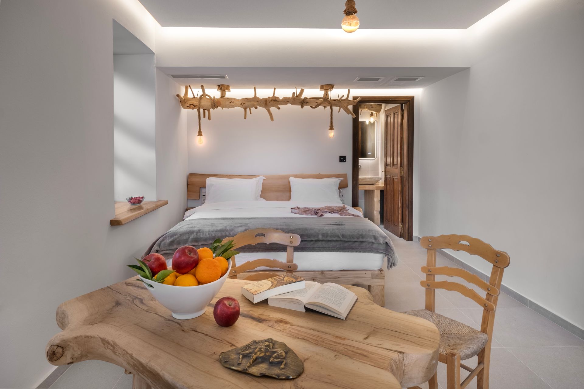 Bedroom with a wooden bed, table with fruit and an open book, and decorative light fixture.
