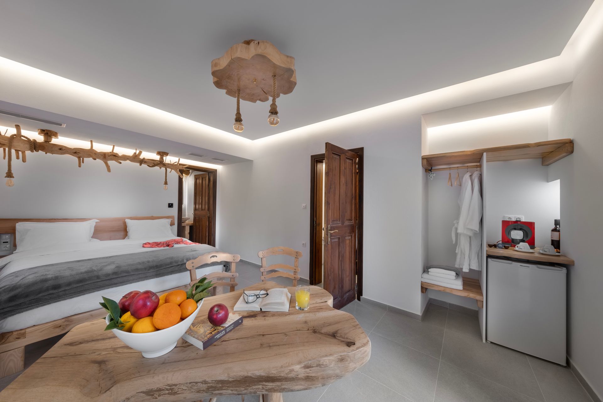 Hotel room with rustic wooden furniture, fruit bowl on table, bed with gray blanket.