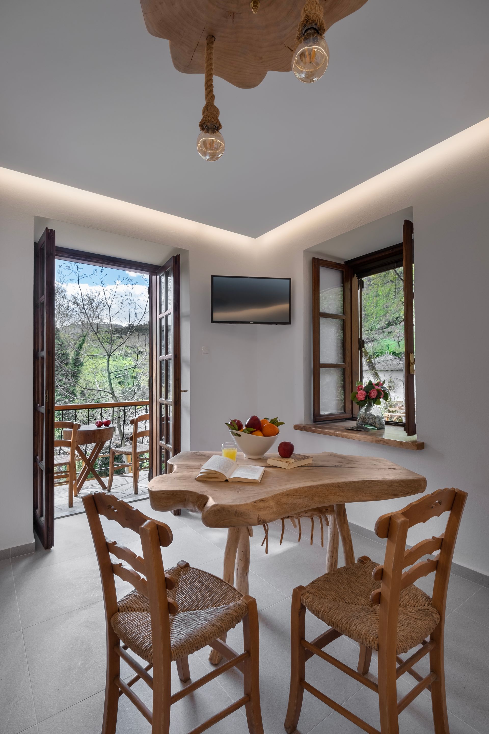 Cozy dining area with wooden table, chairs, and balcony access. Natural light and fruit on table.