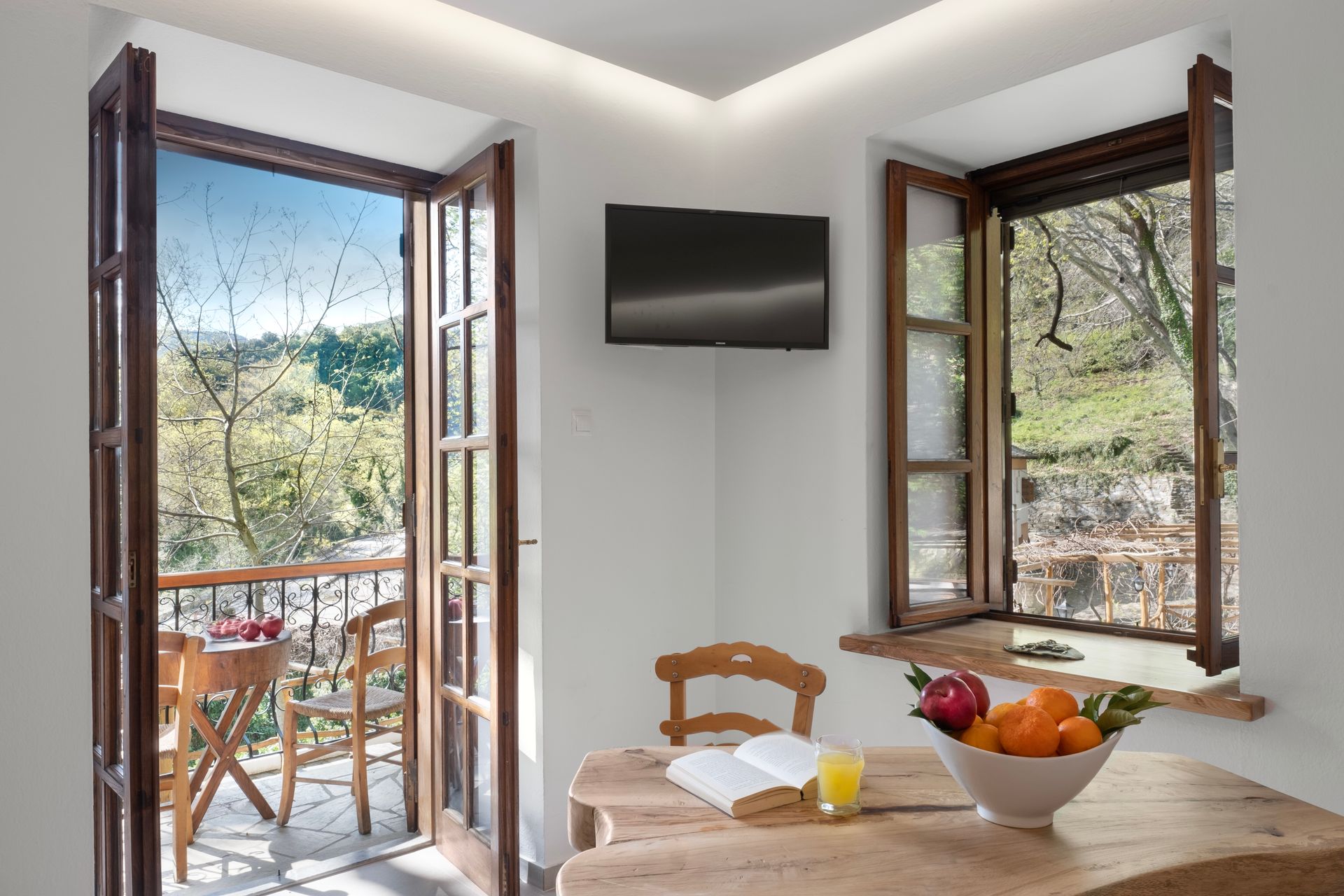 Interior with balcony view, wooden table, and fruit bowl.  Open doors, window, and TV.
