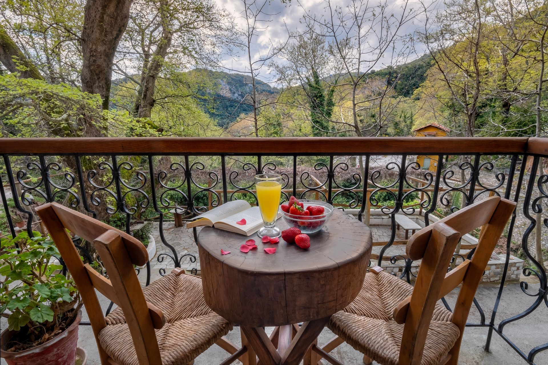 Balcony with round table, chairs, juice, strawberries, and mountain view.