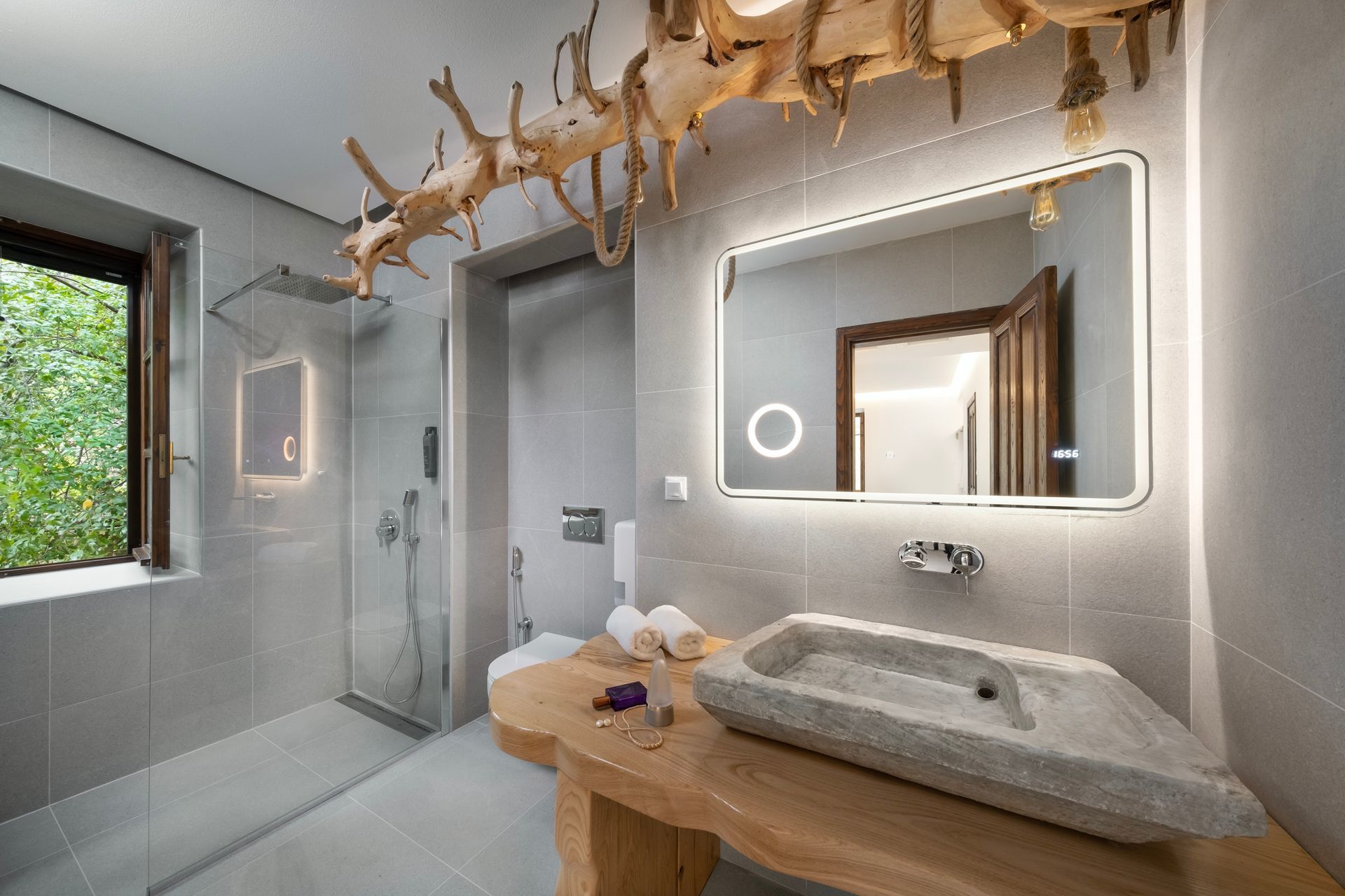 Modern bathroom with stone sink and wood accents. Shower, mirror, and window.