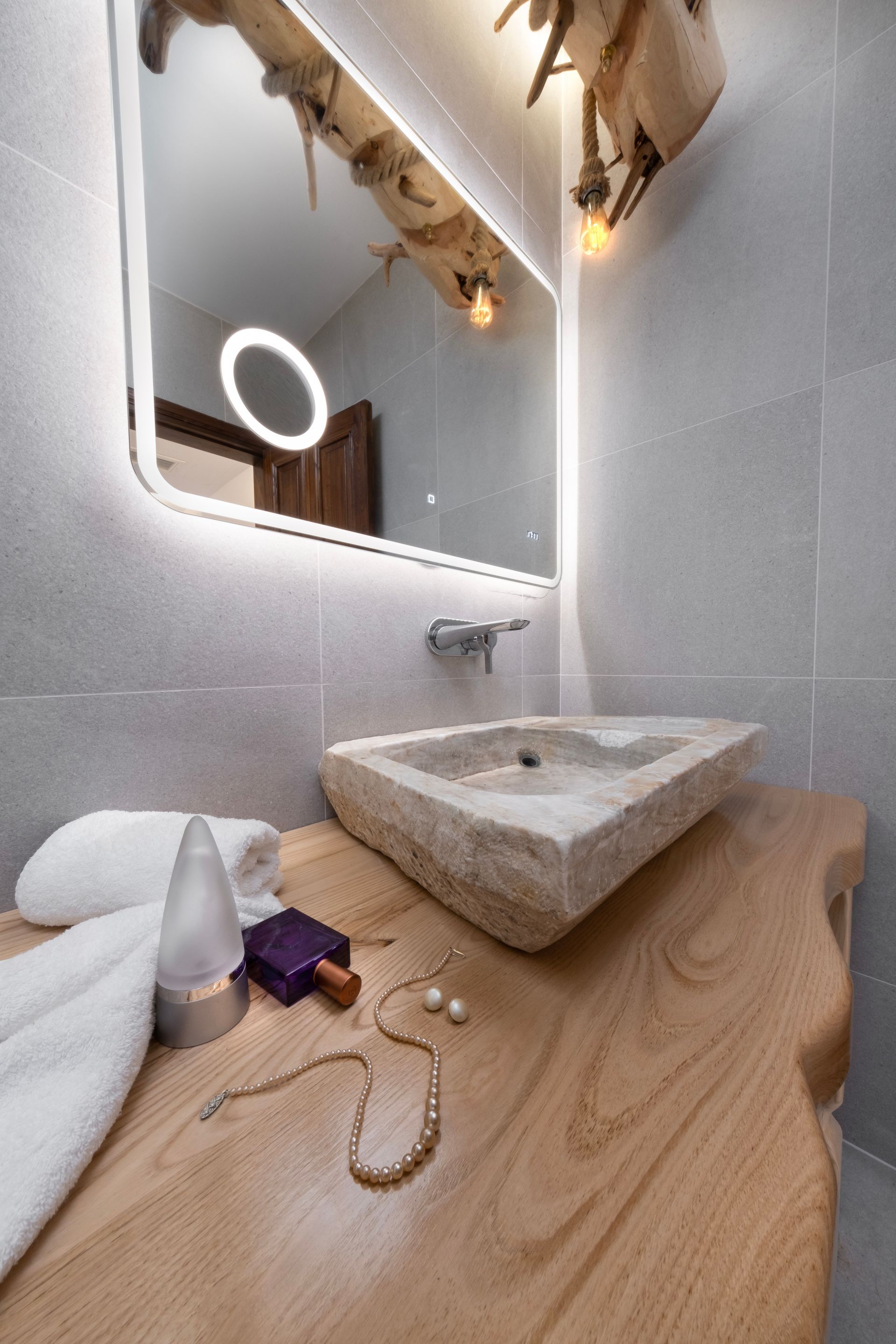Bathroom with a triangular stone sink on a wooden countertop. A lighted mirror reflects the room.