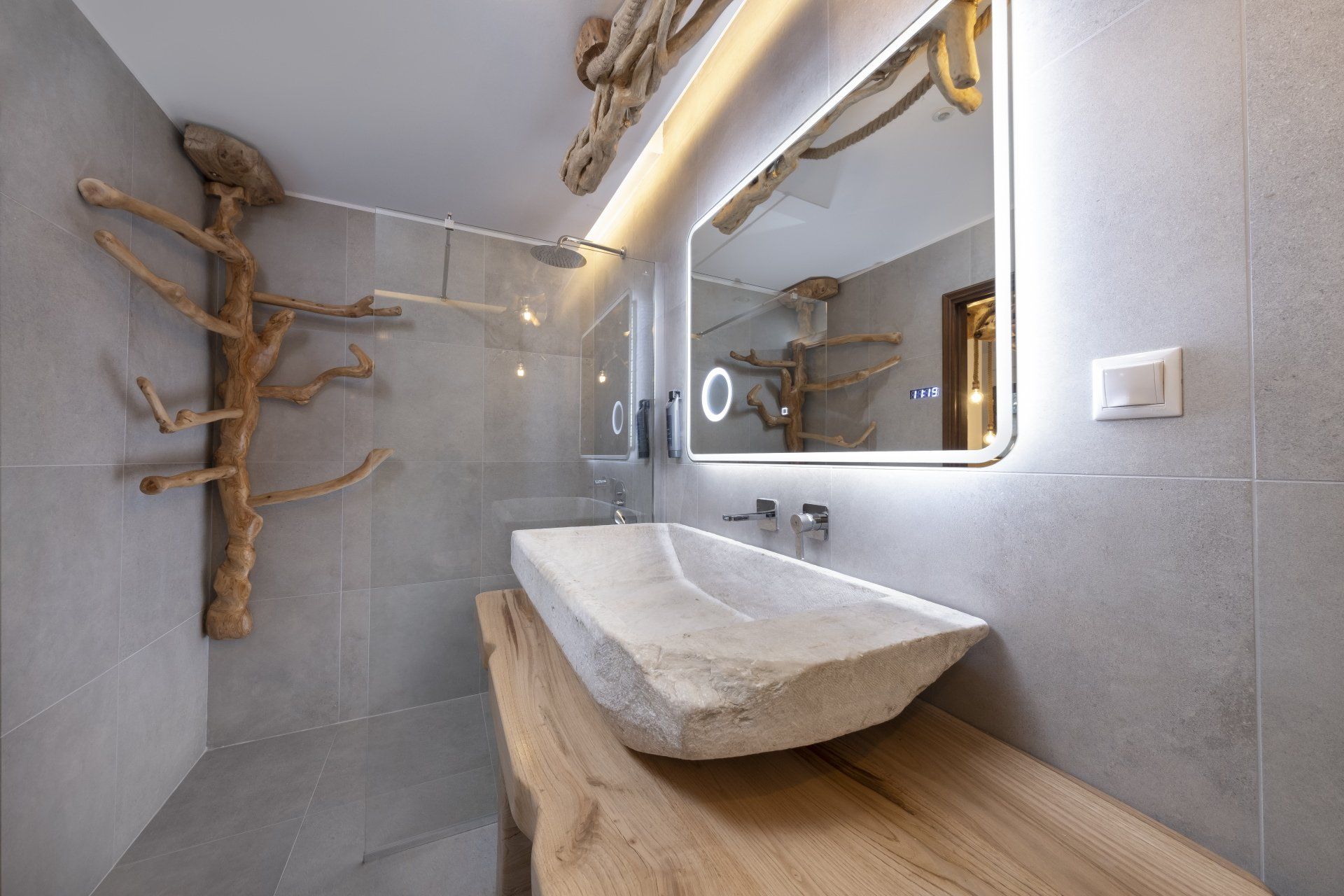 Modern bathroom with stone sink, wooden accents, and gray tiled walls.