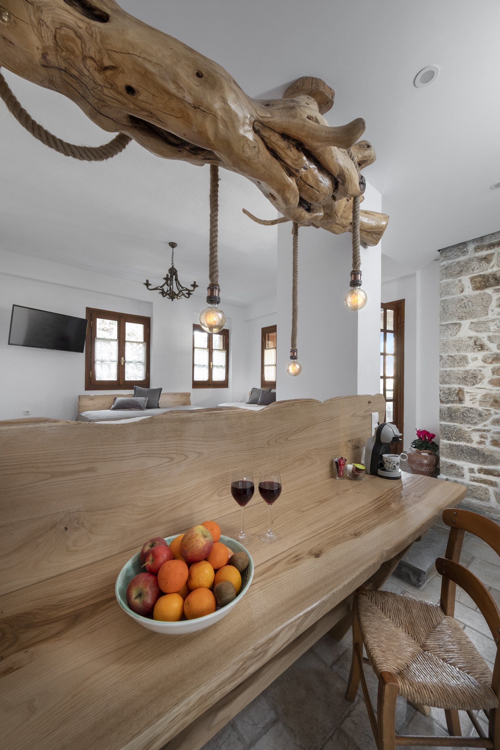 Wooden bar with fruit, wine, and hanging lights. Rustic interior with windows and a stone wall.