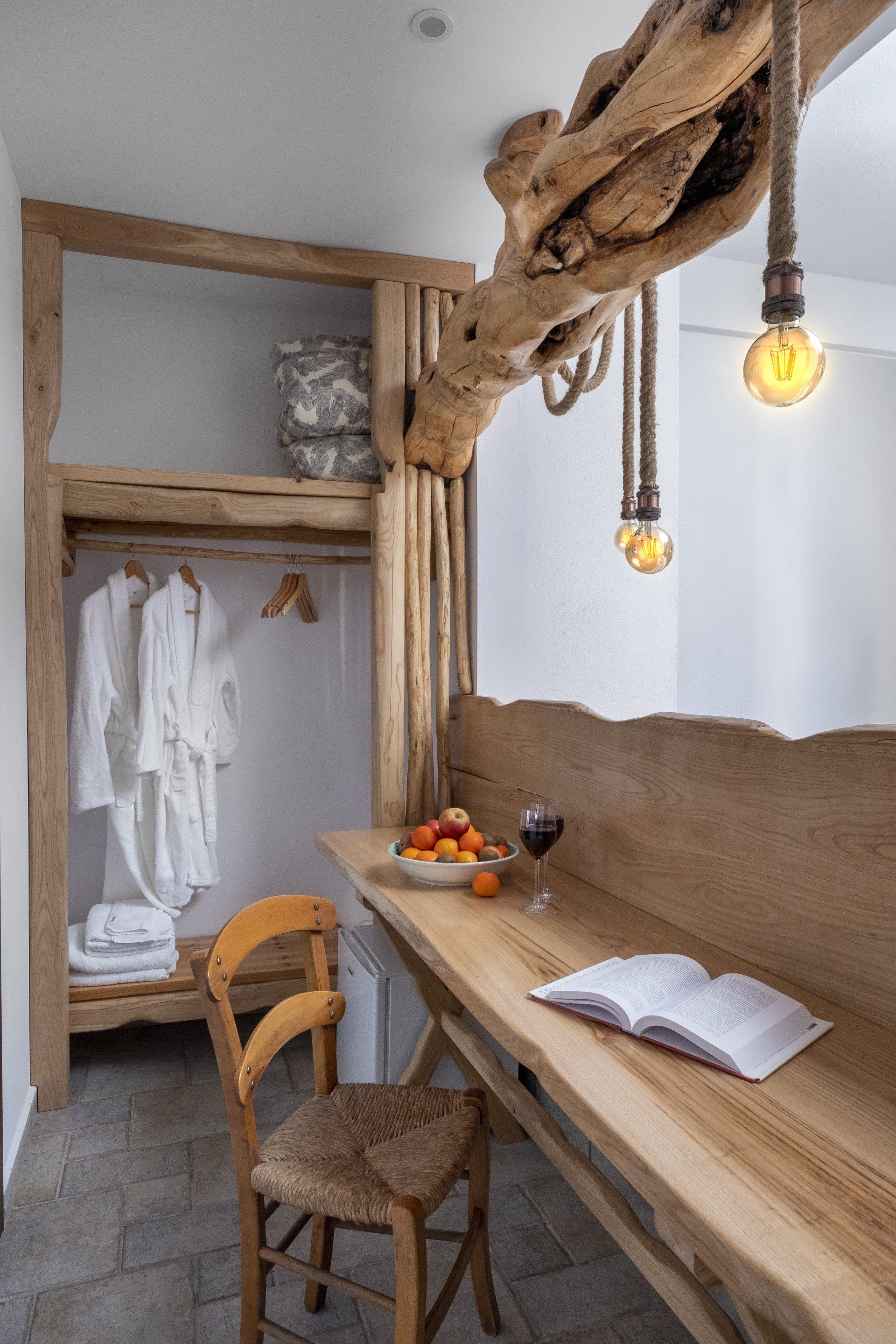 Cozy hotel room with a wooden desk, hanging lights, and a closet with robes.