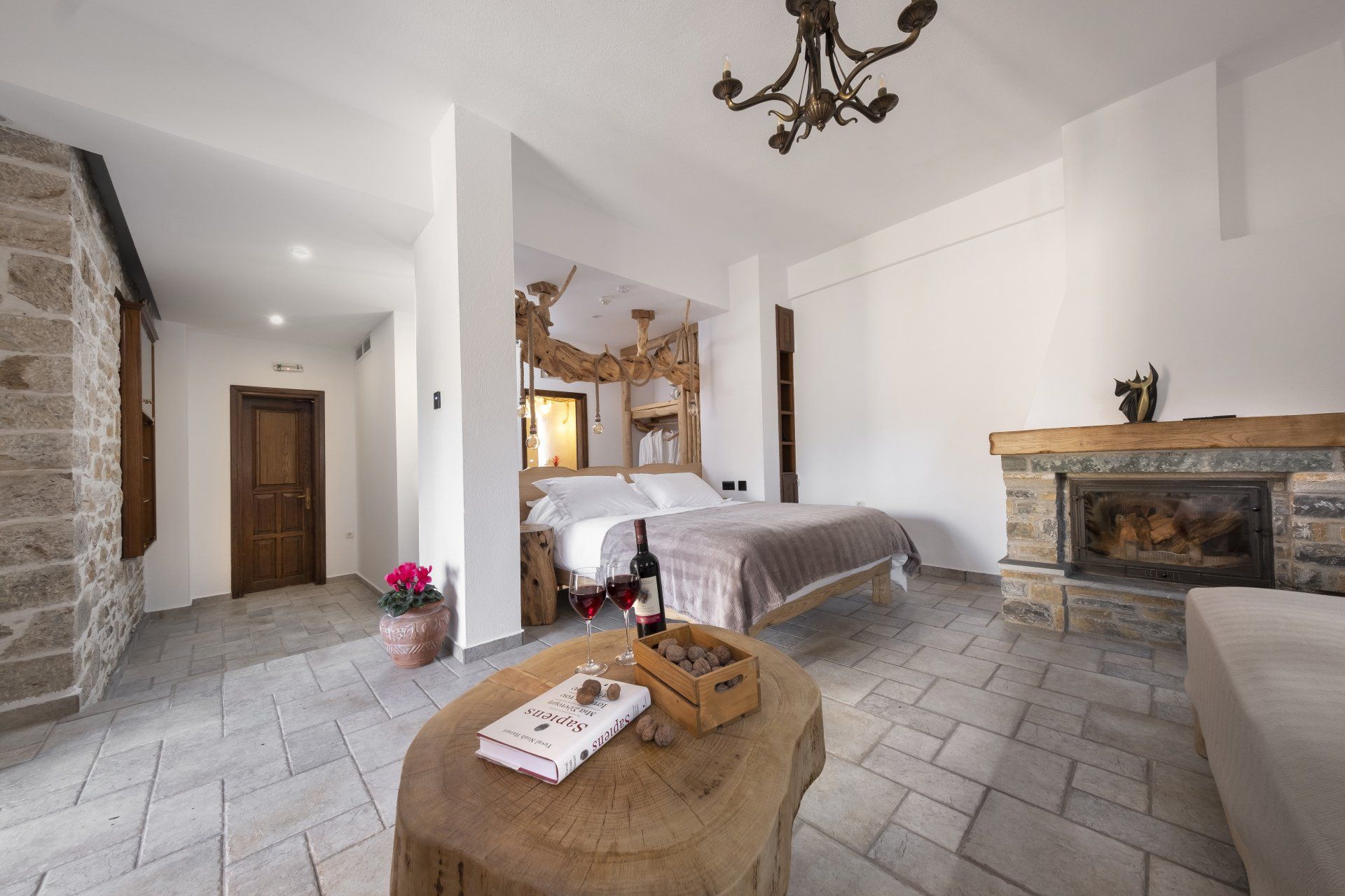 Cozy hotel room with stone walls, fireplace, bed, and wooden table with a book and wine.