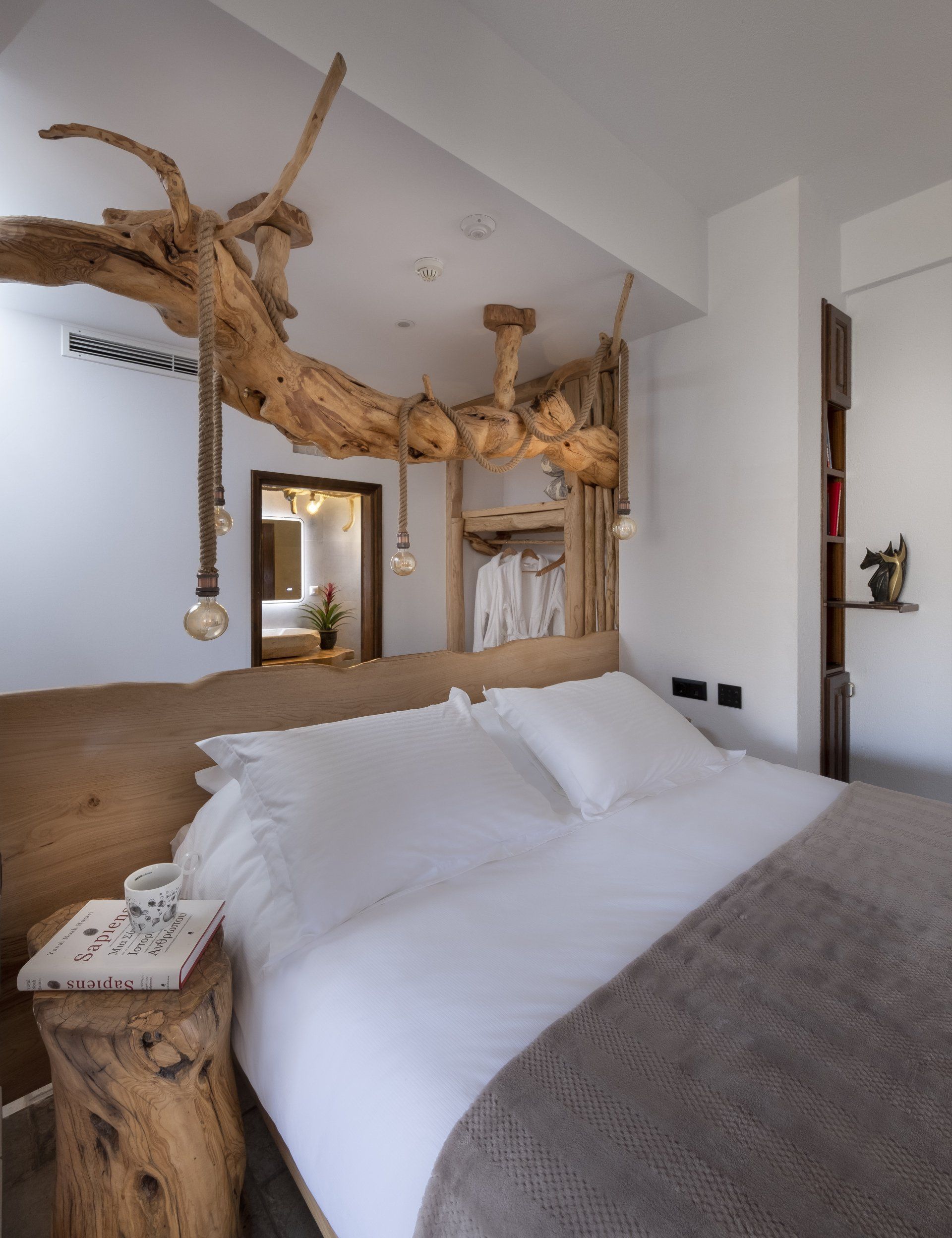 Bedroom with wooden headboard, tree branch decor on ceiling, white bedding, and small side table.