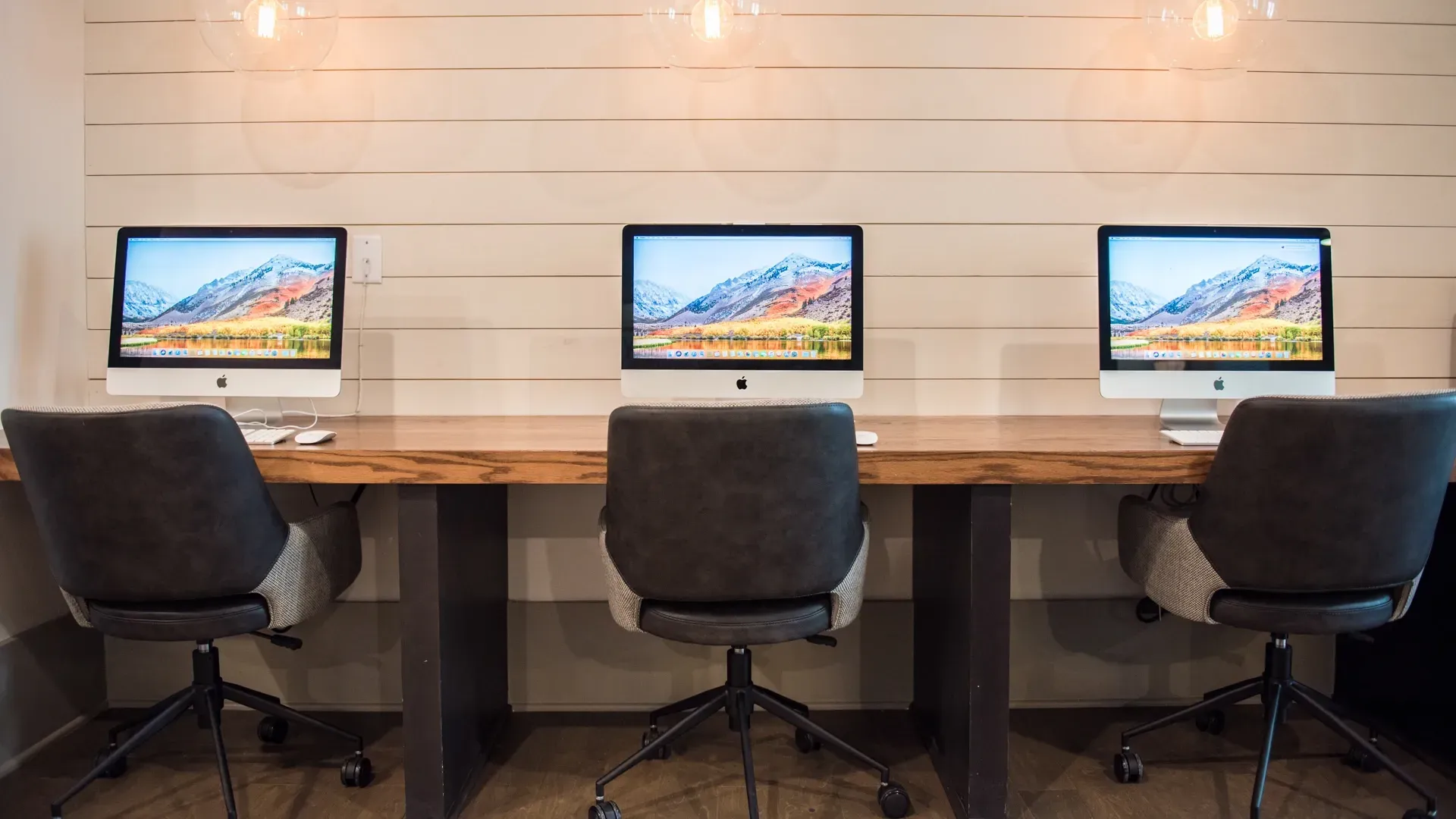 Community business center with three iMac computers on a wooden desk with chairs.