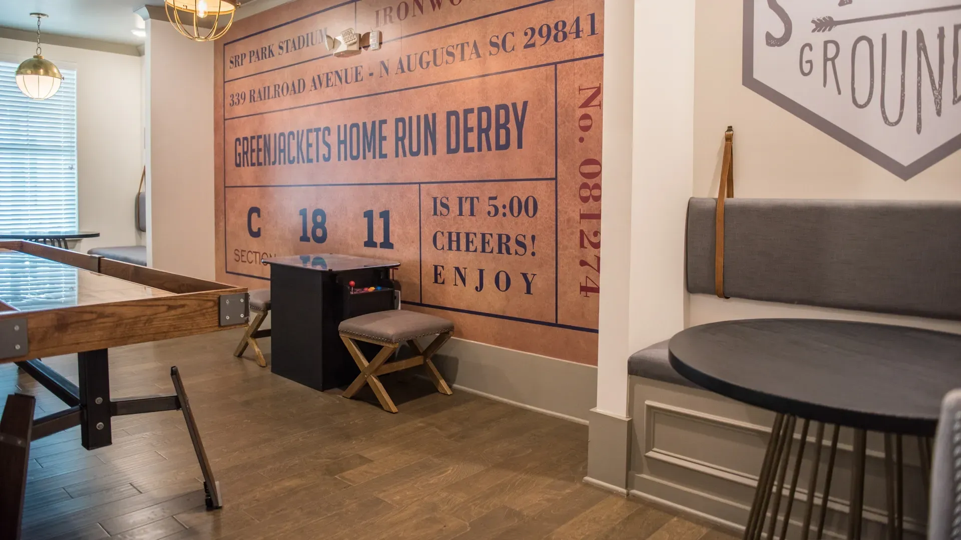 A community lounge area with a foosball table, arcade game, and ticket-themed mural.