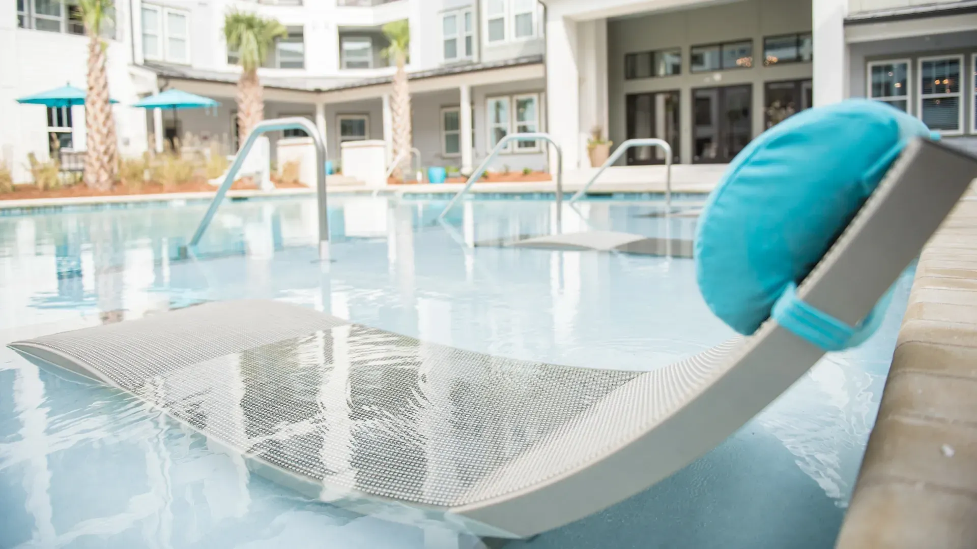 In-water chaise lounge with turquoise cushion in a swimming pool.